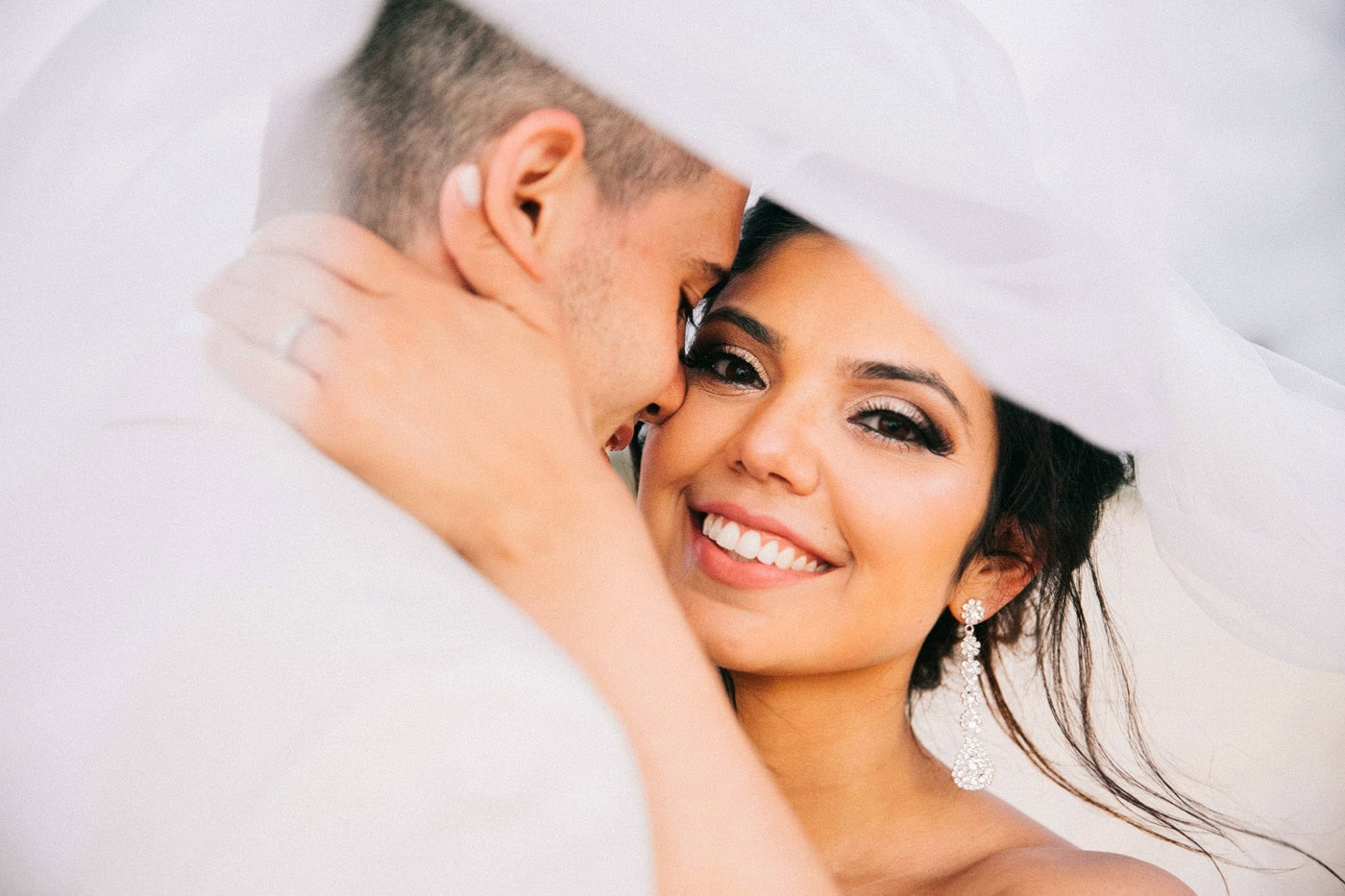 Bride smiling as her groom kisses her cheek under her wedding veil during their Punta Cana wedding
