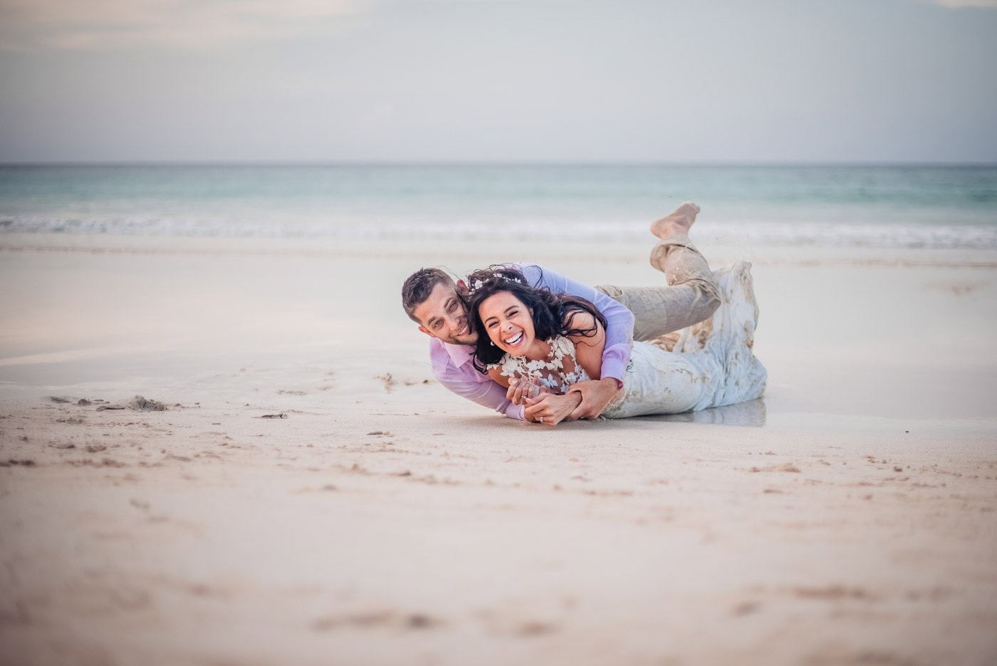 Bride and groom laughing together while lying on the sand during a beach photo session in Punta Cana