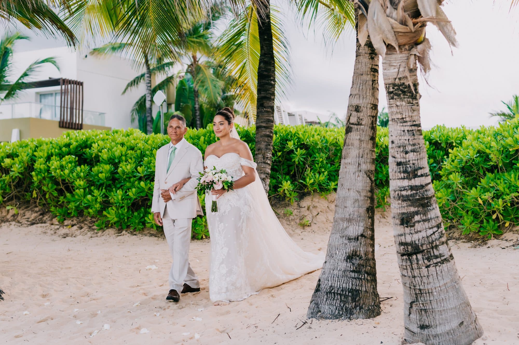 Father walking the bride toward her beach ceremony past the palms at Dreams Onyx