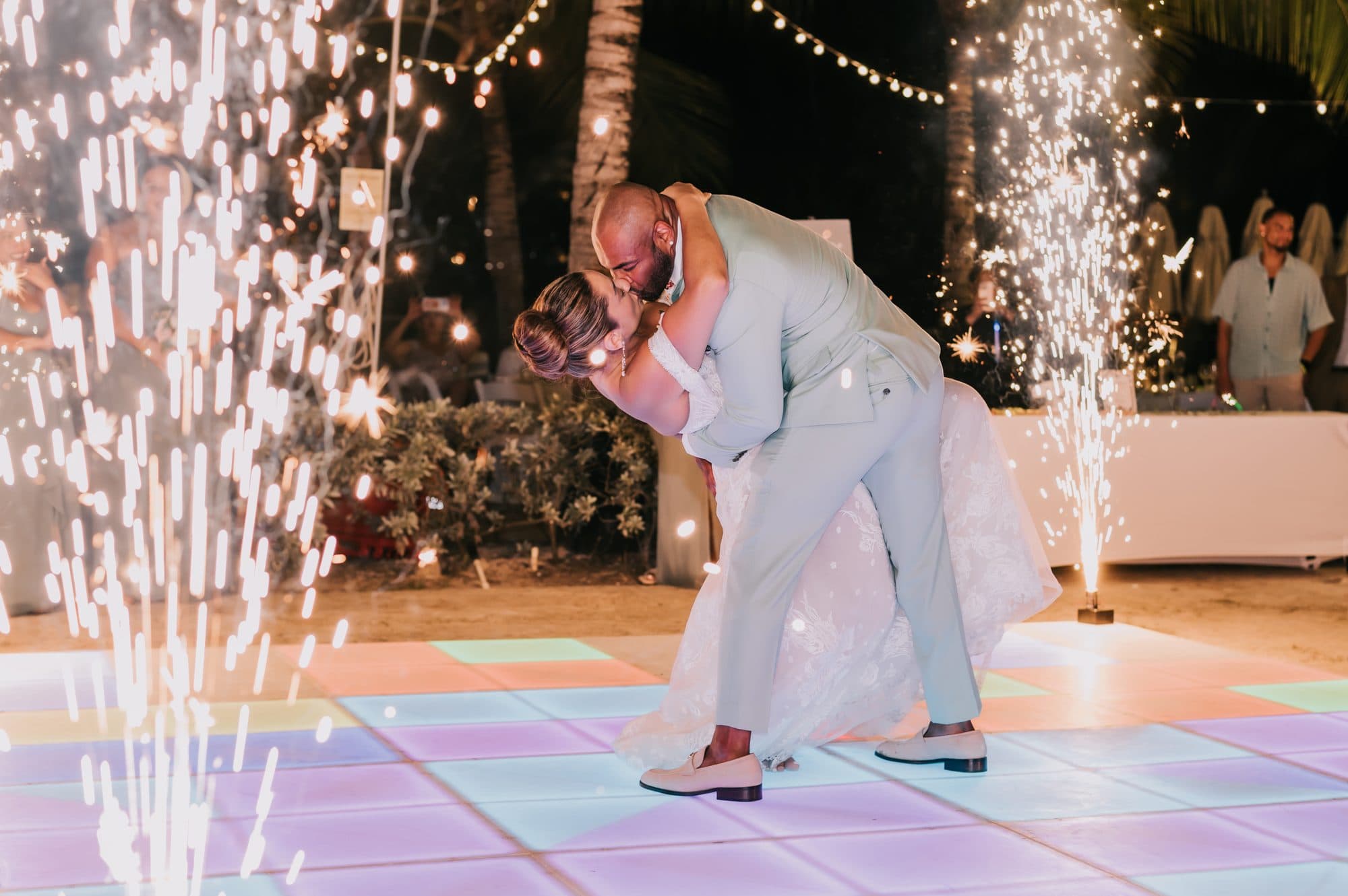 Groom dipping the bride for a kiss surrounded by cold-spark fountains on the reception dance floor at Dreams Onyx