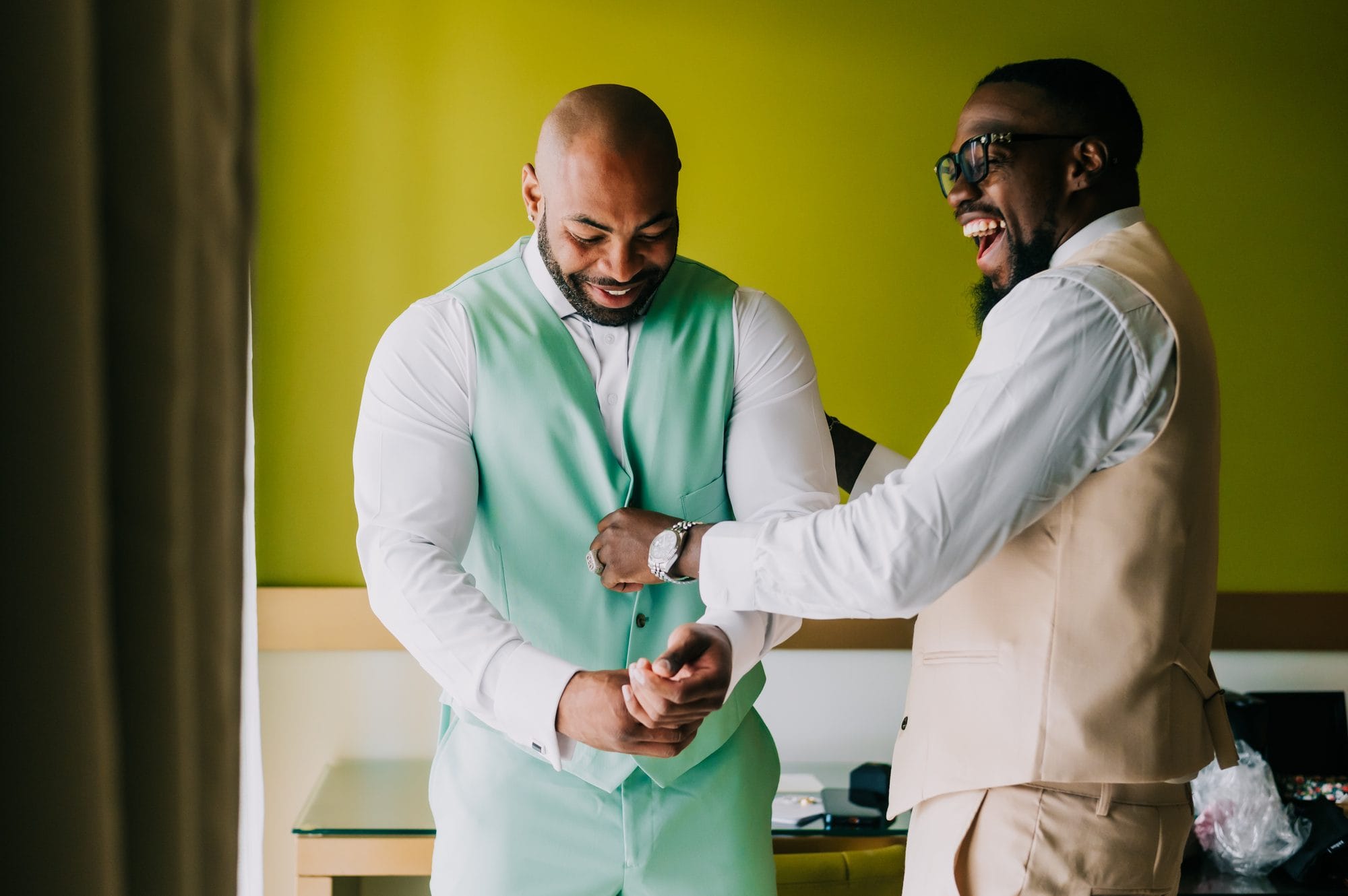 Groom and groomsman laughing while fastening cufflinks before the beach ceremony at Dreams Onyx