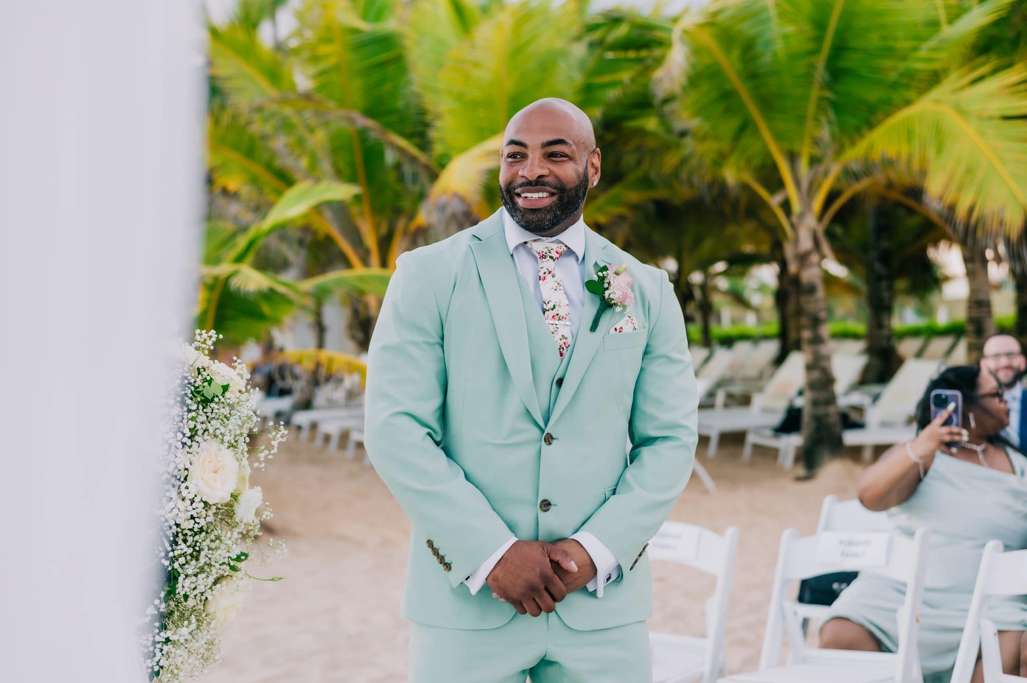 Groom in a mint suit smiling as he waits at the beach altar at Dreams Onyx Punta Cana