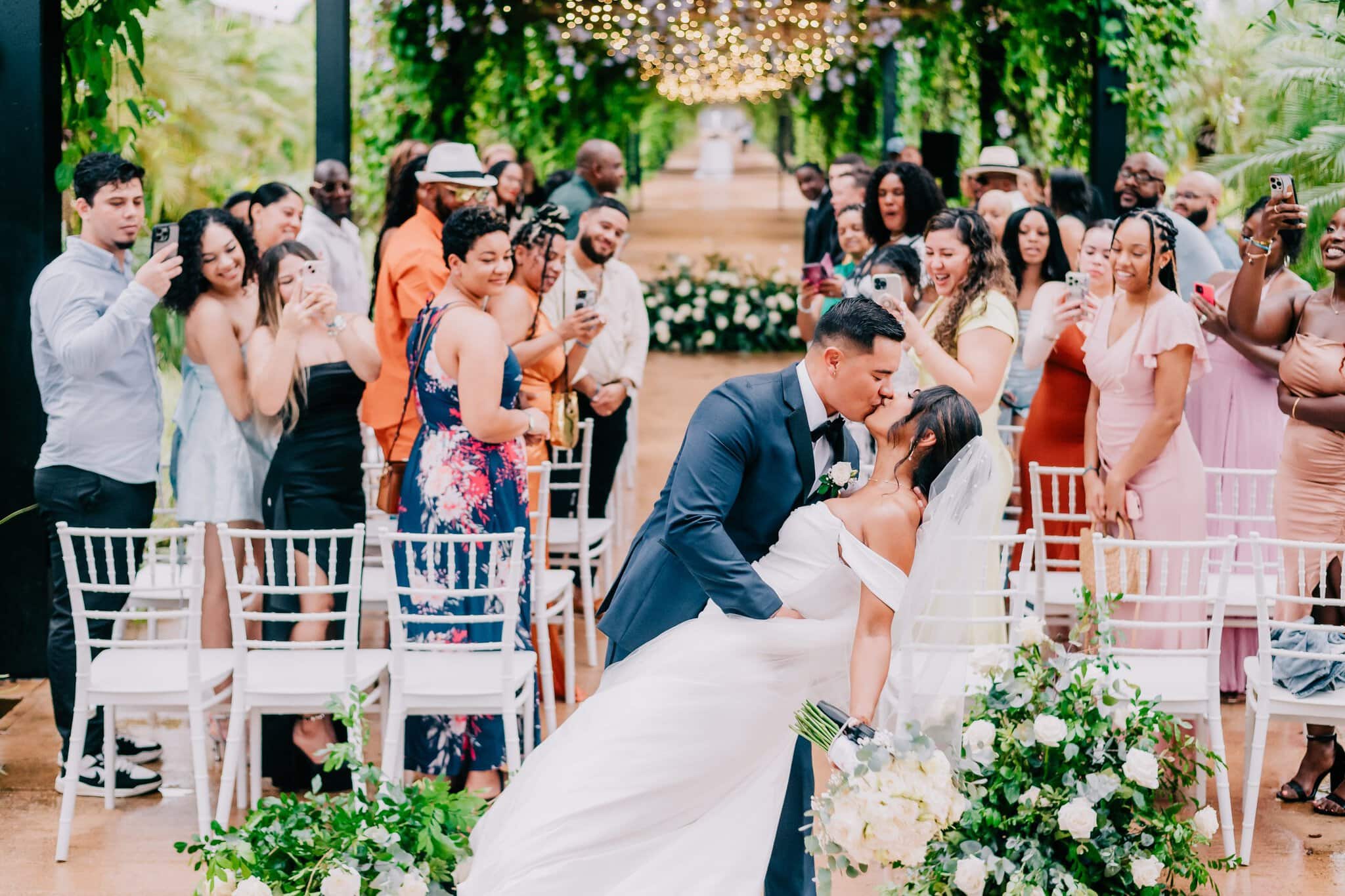 Bride and groom sharing a kiss under the greenery and string lights at Live Aqua Punta Cana