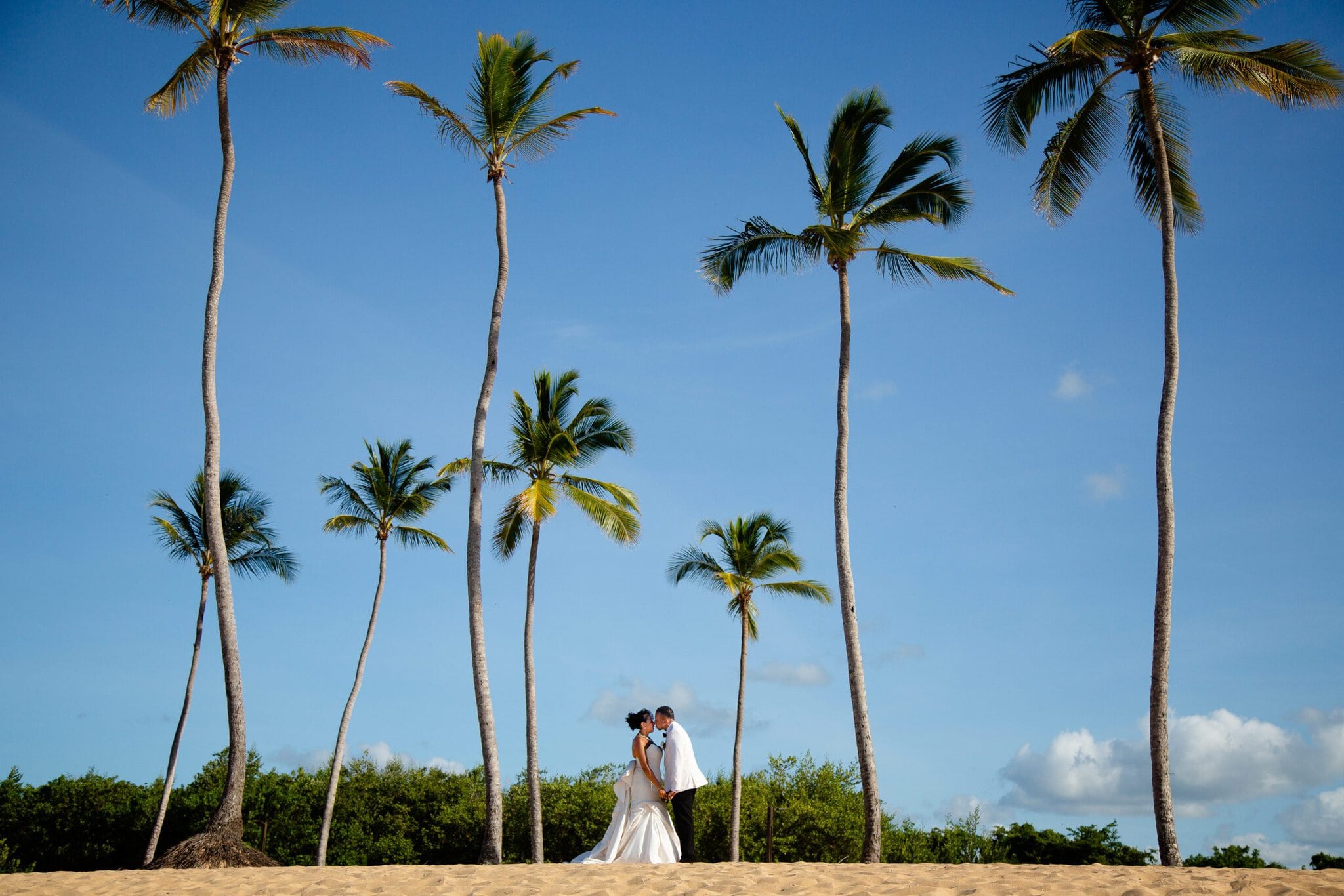 A couple stand face to face on a Punta Cana beach framed by palm trees in soft evening light.