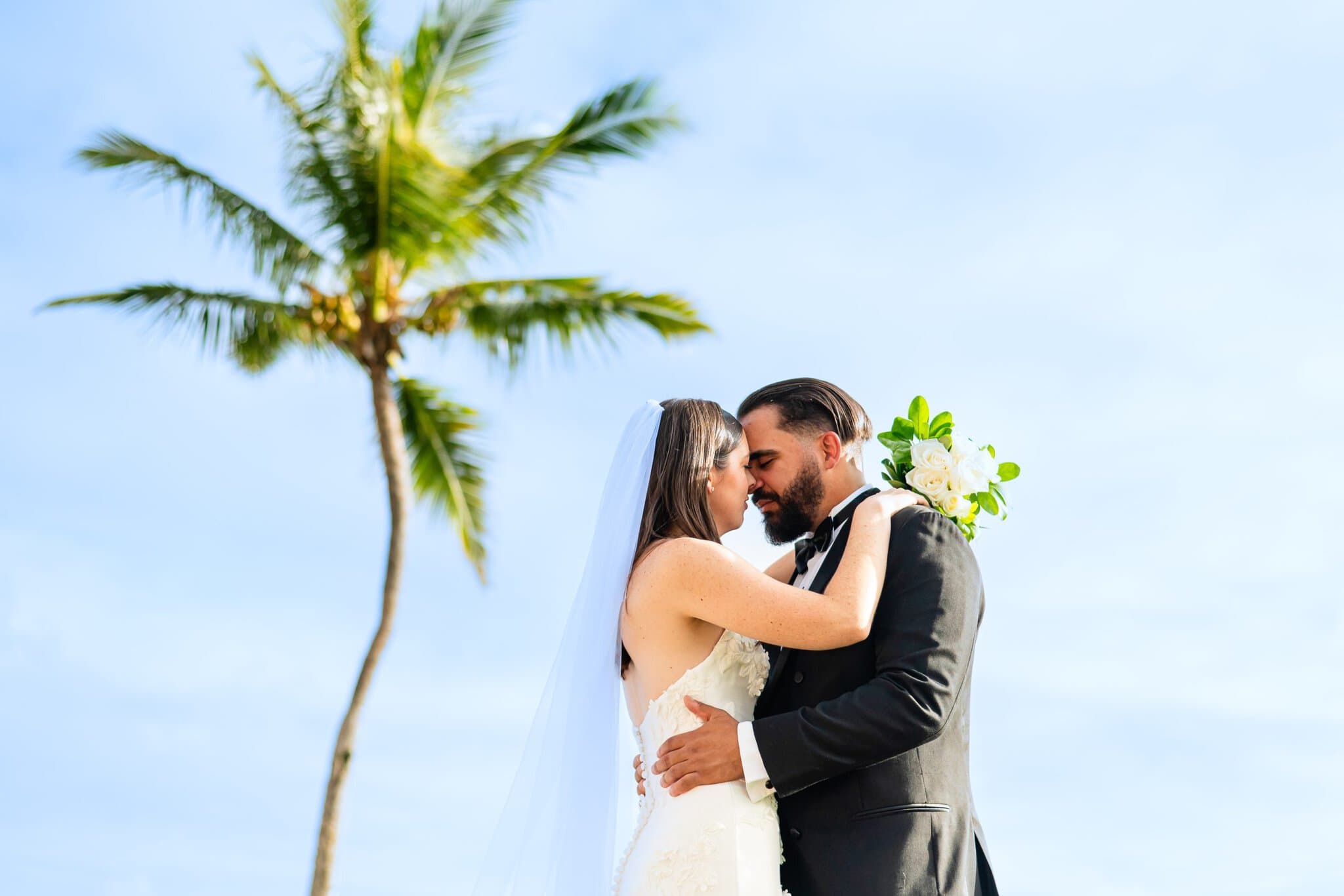 Bride and groom embracing under a palm tree at their Punta Cana destination wedding