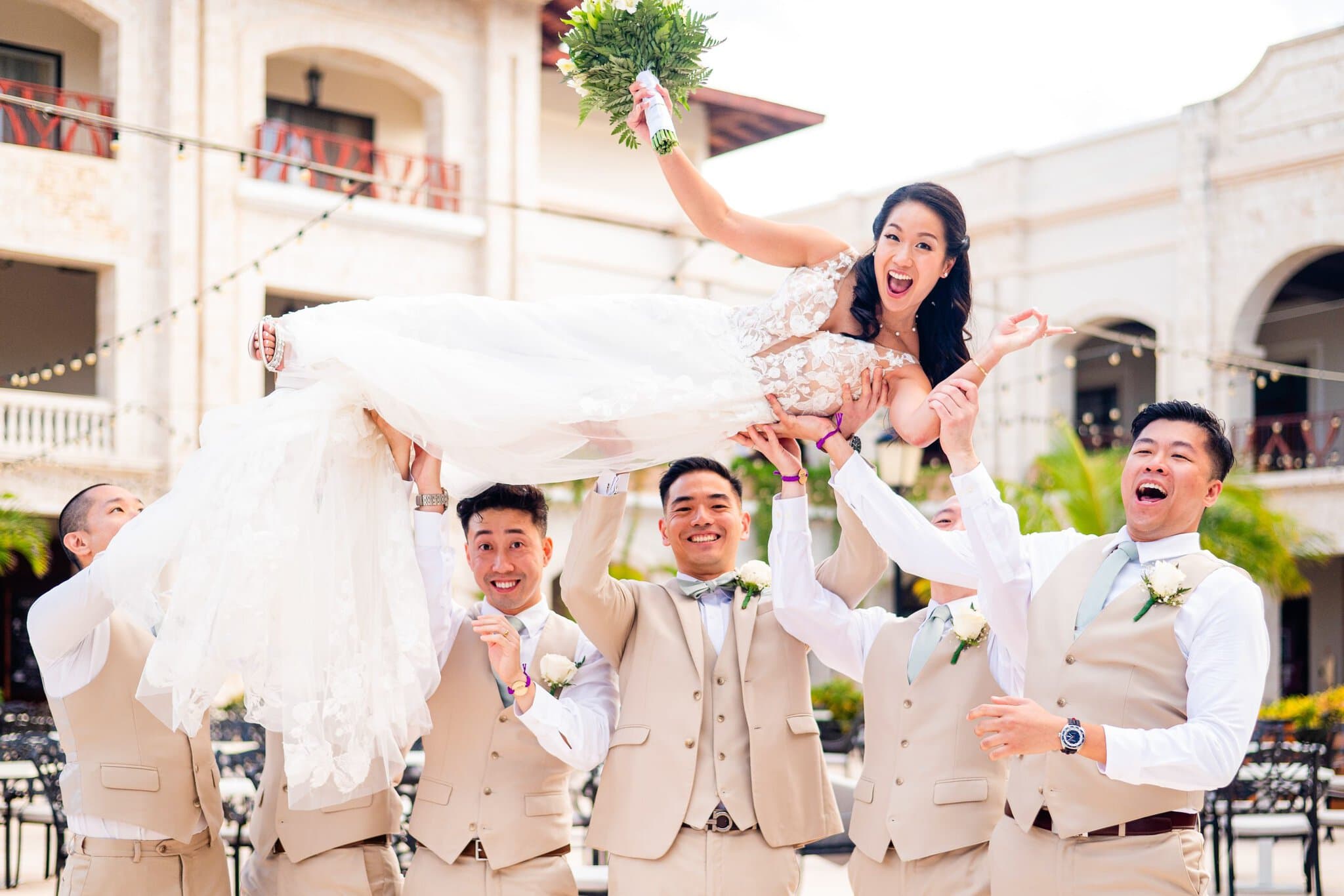 Groomsmen lifting the laughing bride in the air at a Punta Cana resort wedding