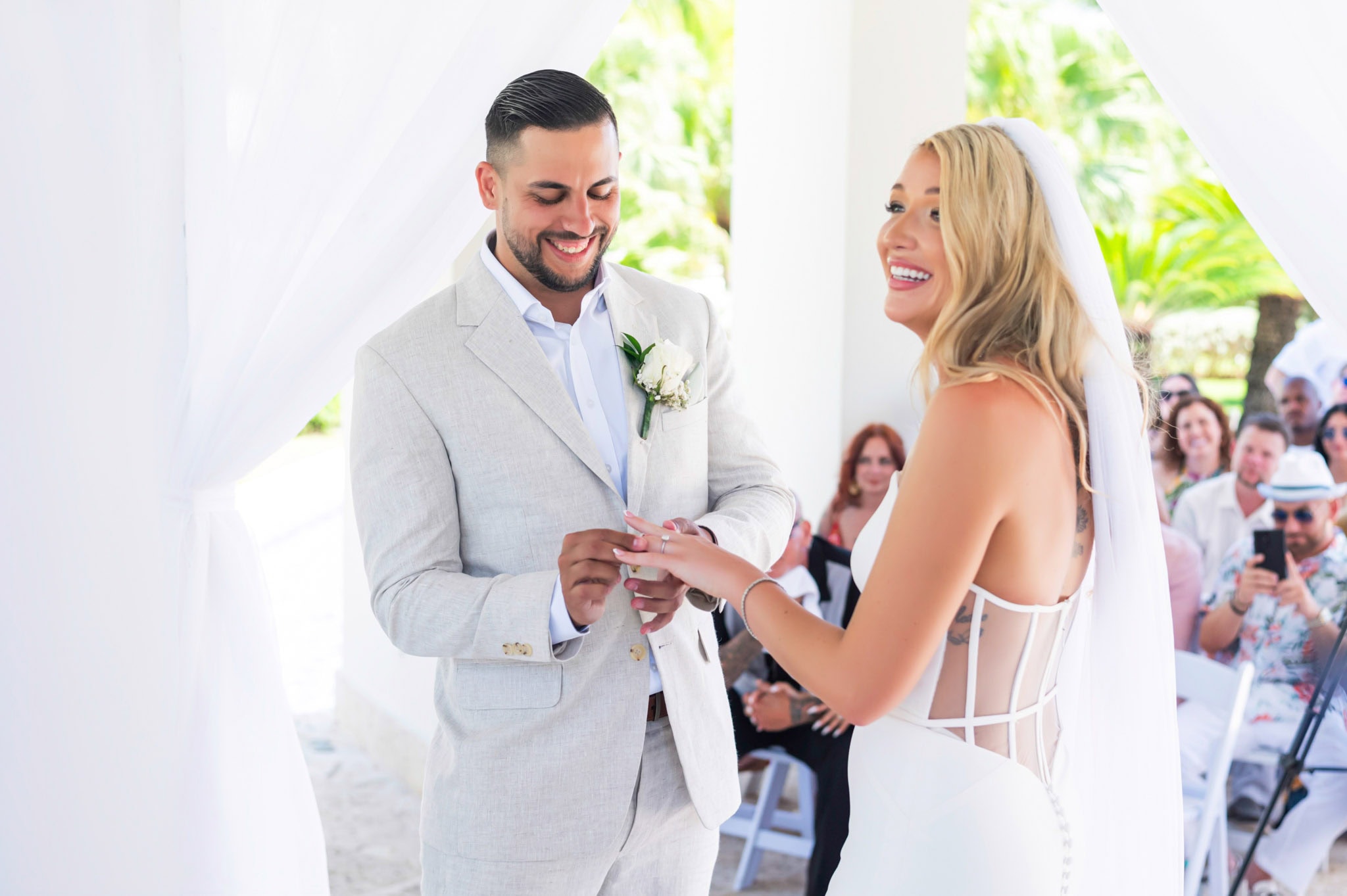 Bride and groom smiling as they exchange rings during their tropical resort wedding ceremony.