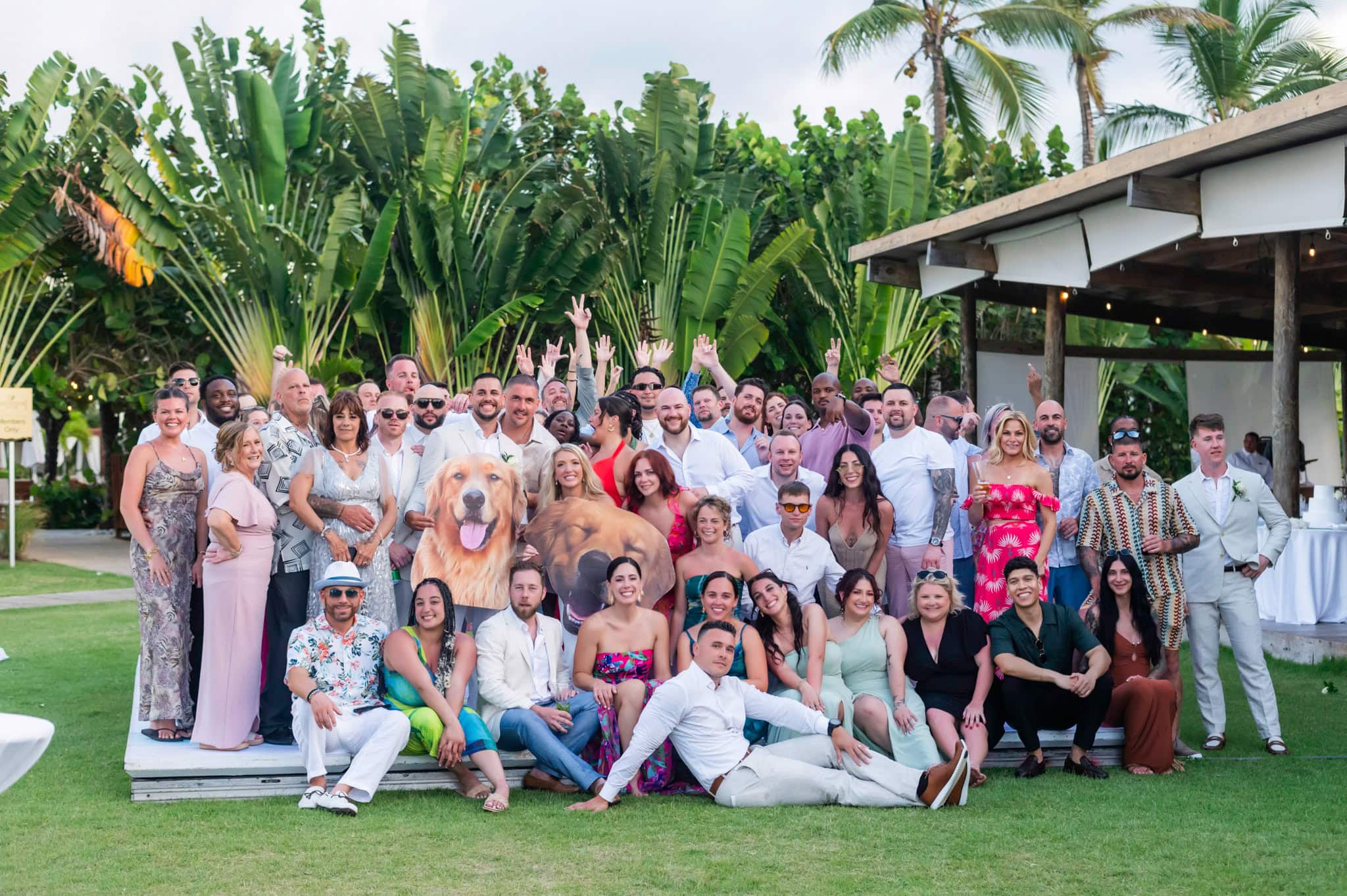 Large wedding group posing with the newlyweds in a tropical resort garden.