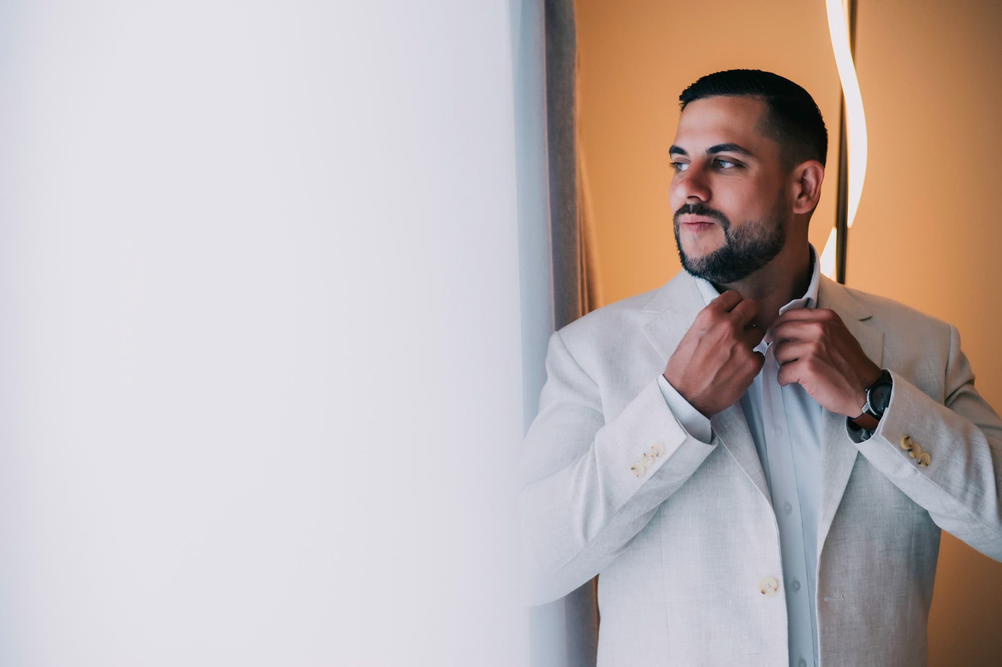 Groom adjusting his tie beside a bright window before the wedding ceremony.