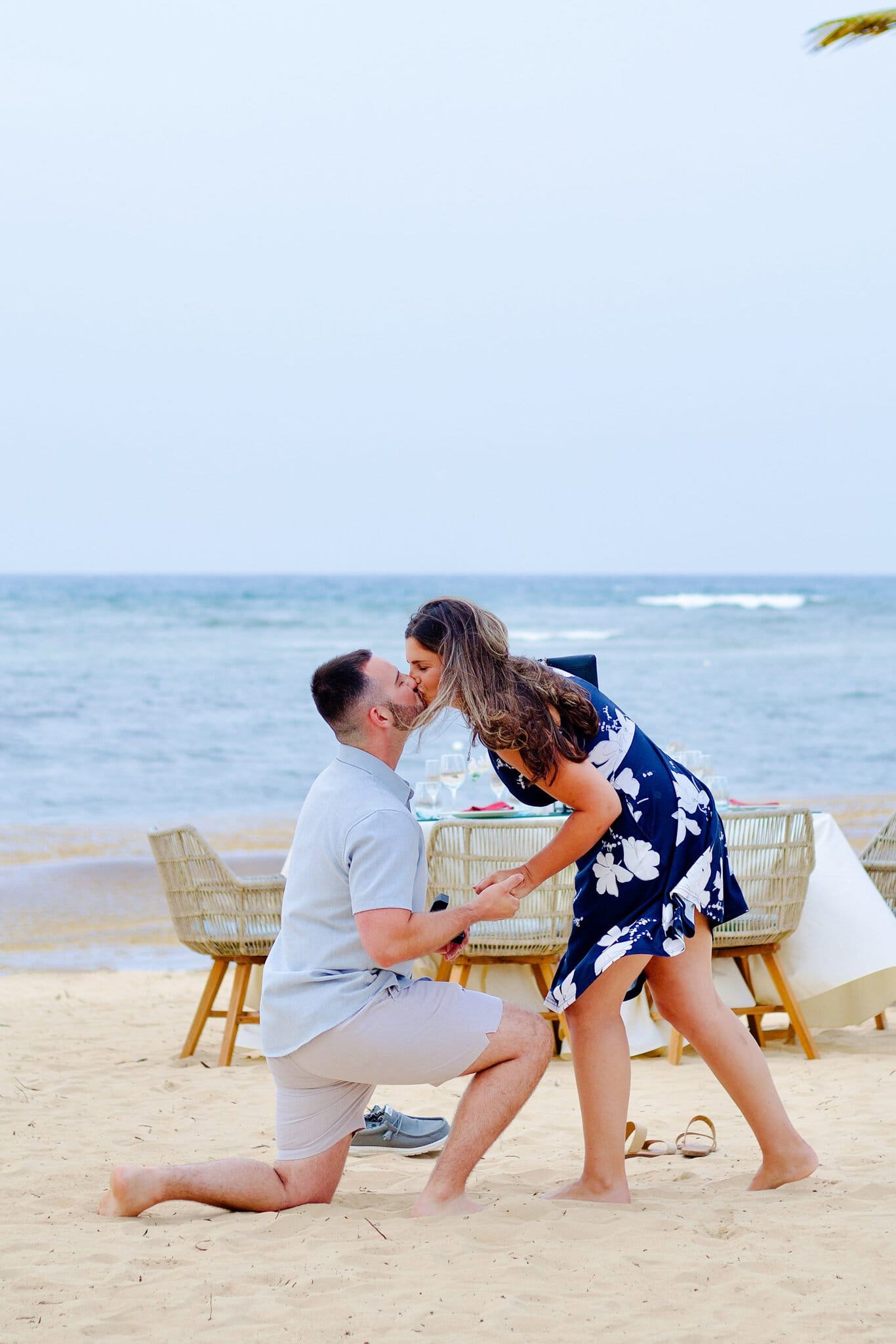Woman leaning down to kiss her partner as he proposes on one knee on the beach at Live Aqua Punta Cana
