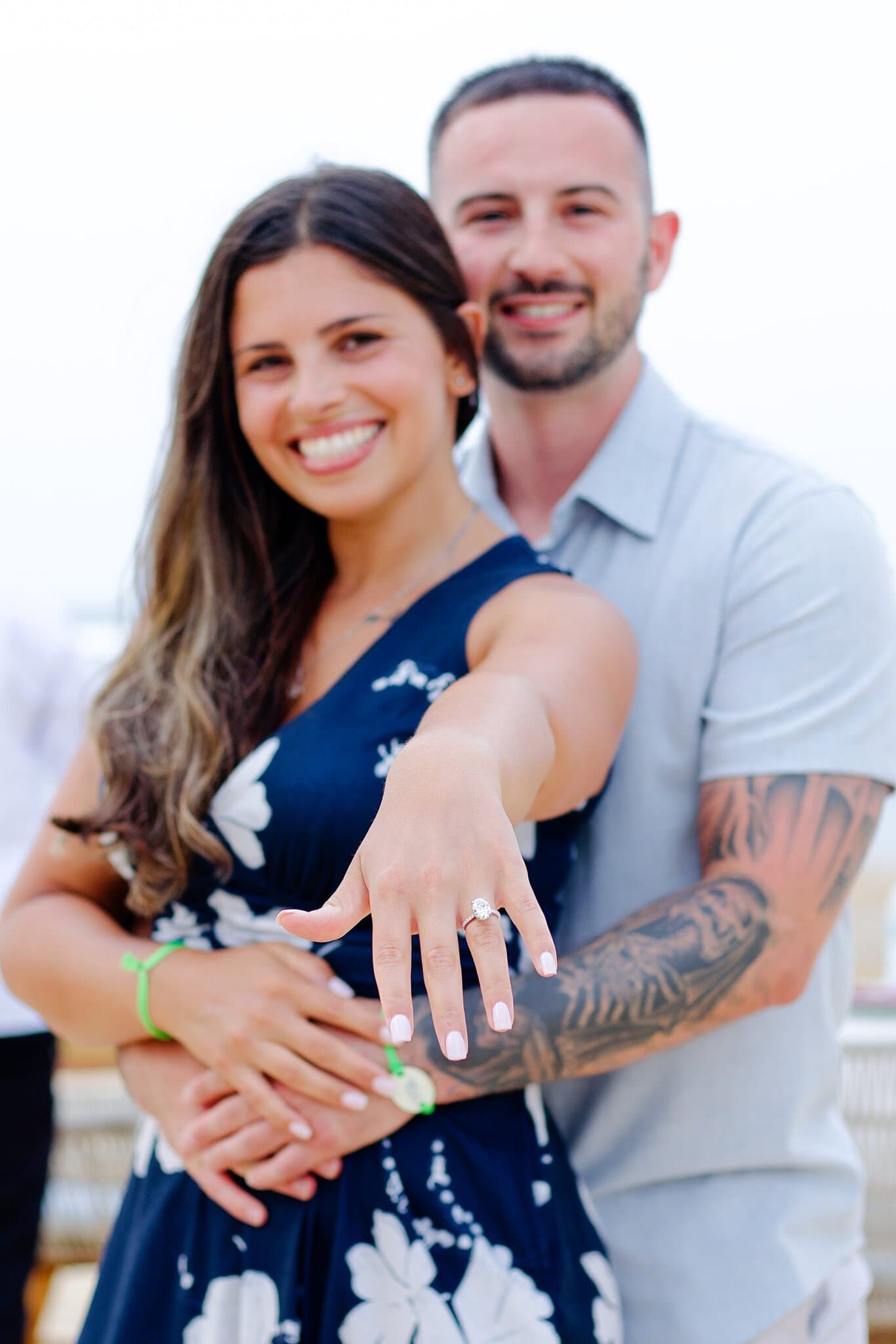 Newly engaged woman showing her engagement ring to the camera while her fiance hugs her from behind