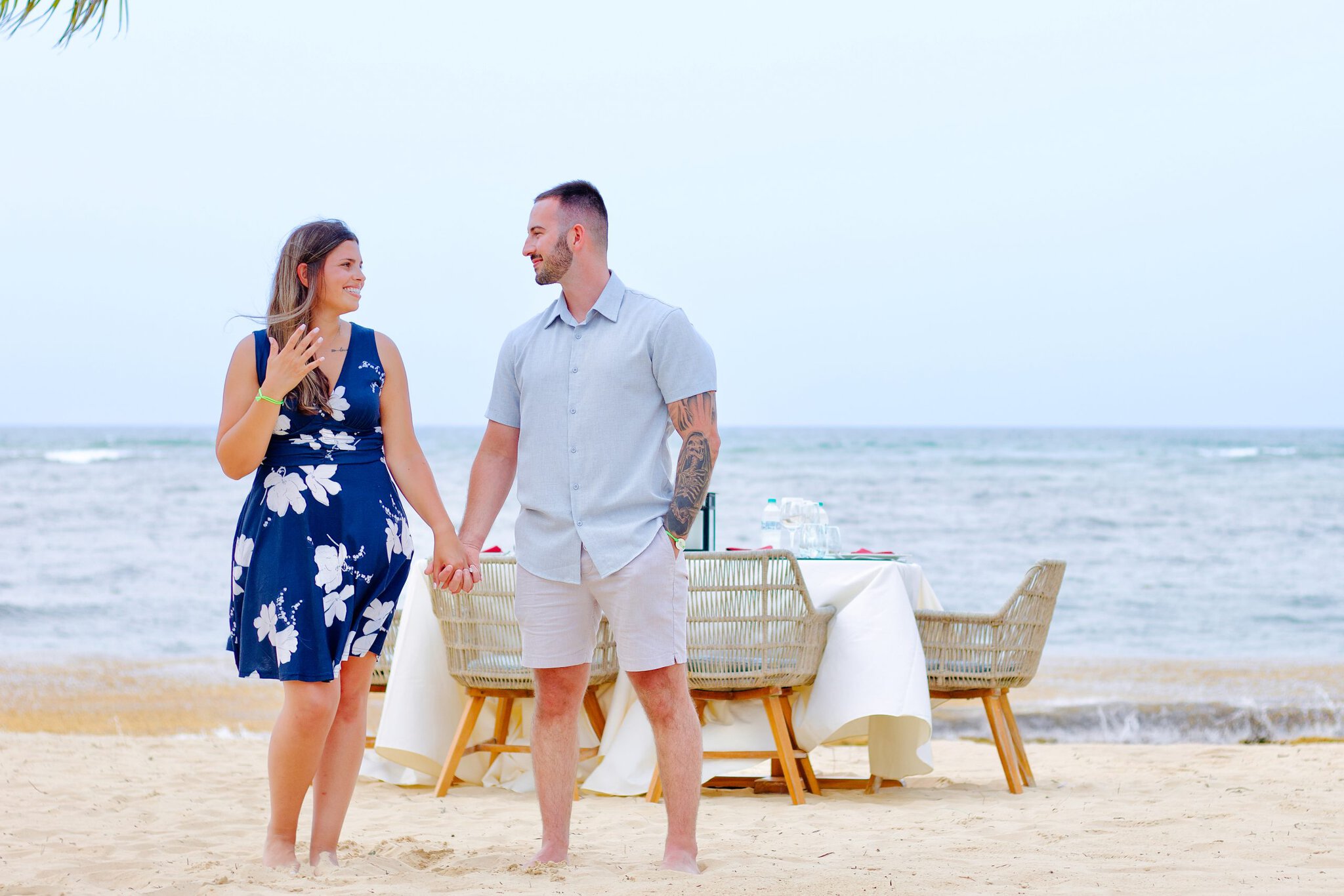 Couple holding hands beside a romantic dinner table for two set on the beach facing the ocean at Live Aqua Punta Cana