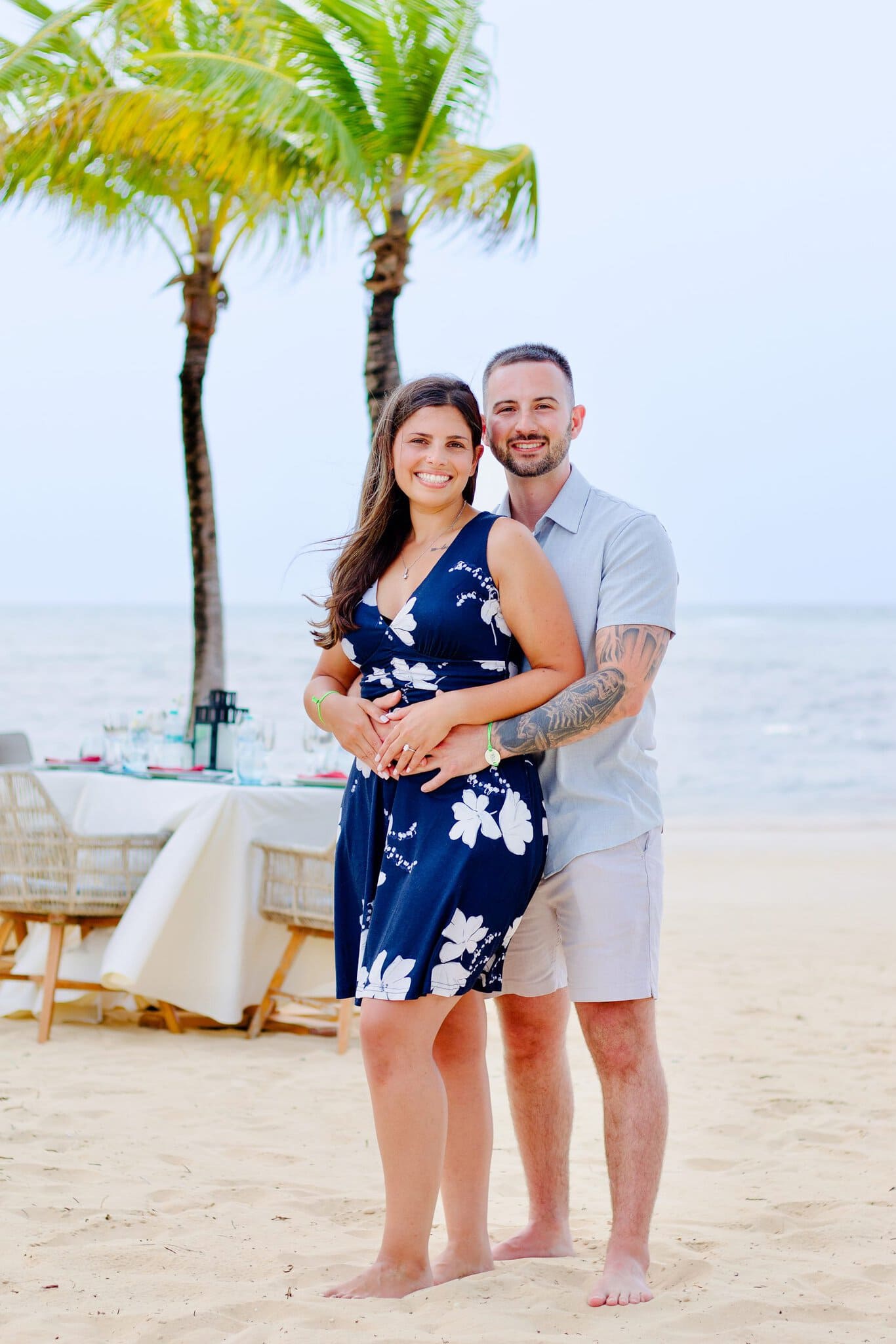 Portrait of a newly engaged couple beside their sunset dinner setup on the beach at Live Aqua Punta Cana