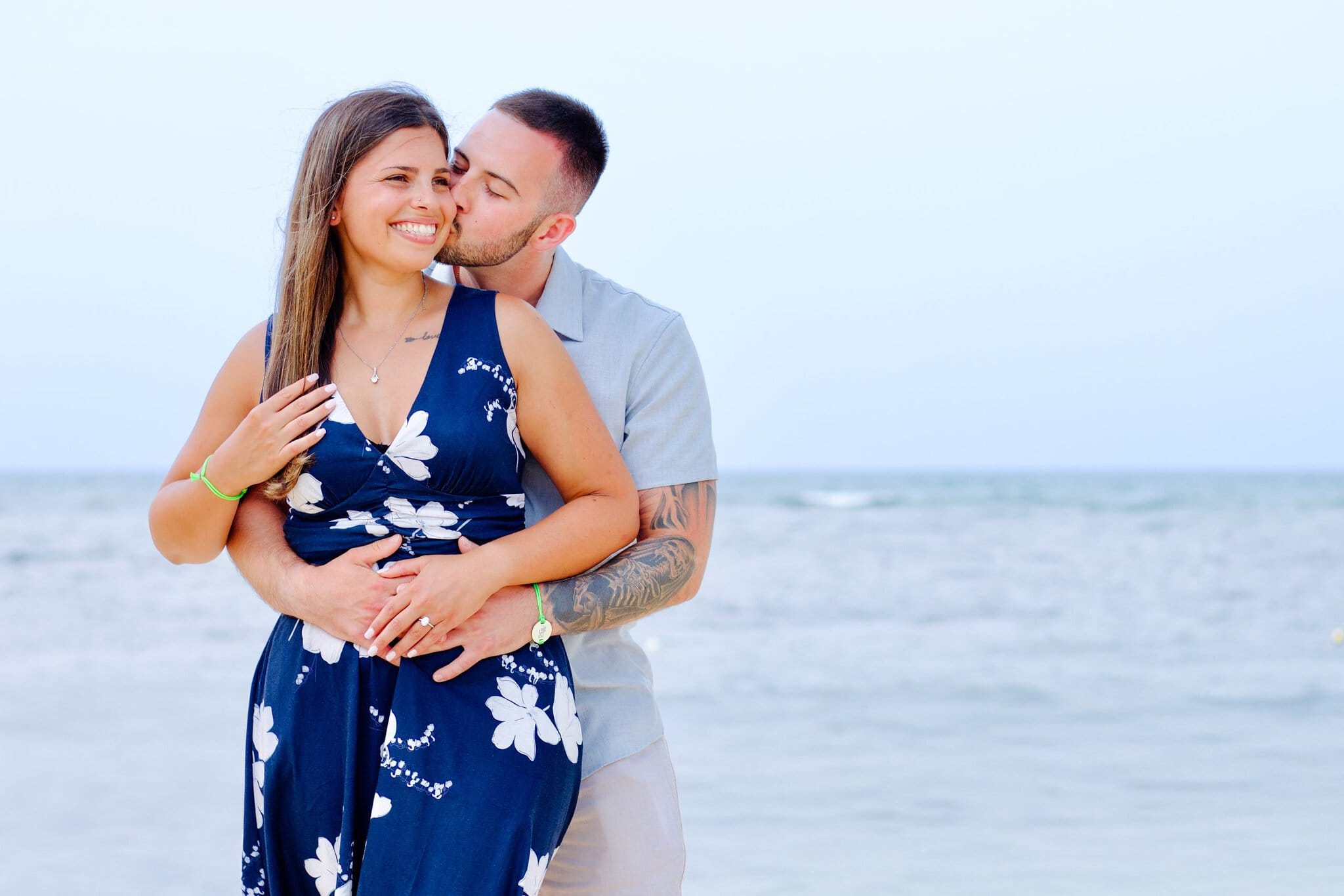 Man kissing his fiancee on the cheek with the Caribbean behind them