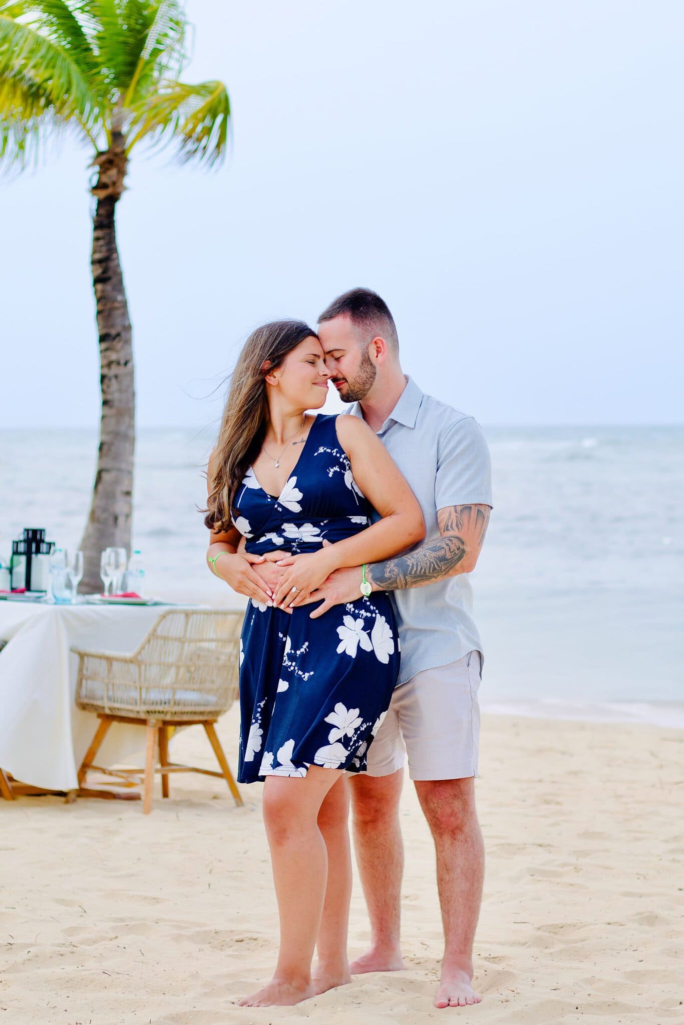 Engaged couple forehead to forehead beside a lantern-lit dinner table on the sand
