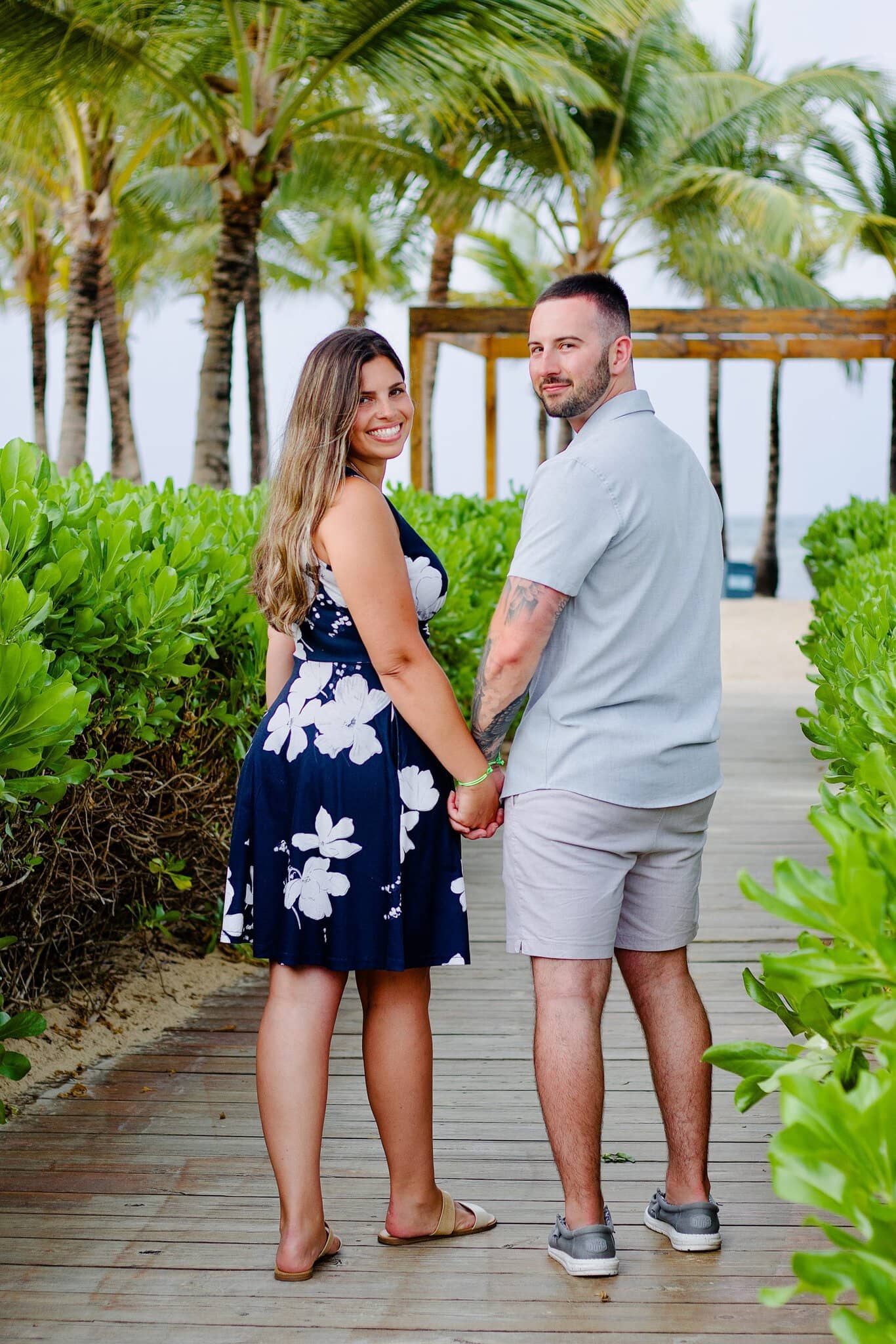 Engaged couple on a palm-lined resort walkway as the woman looks back over her shoulder