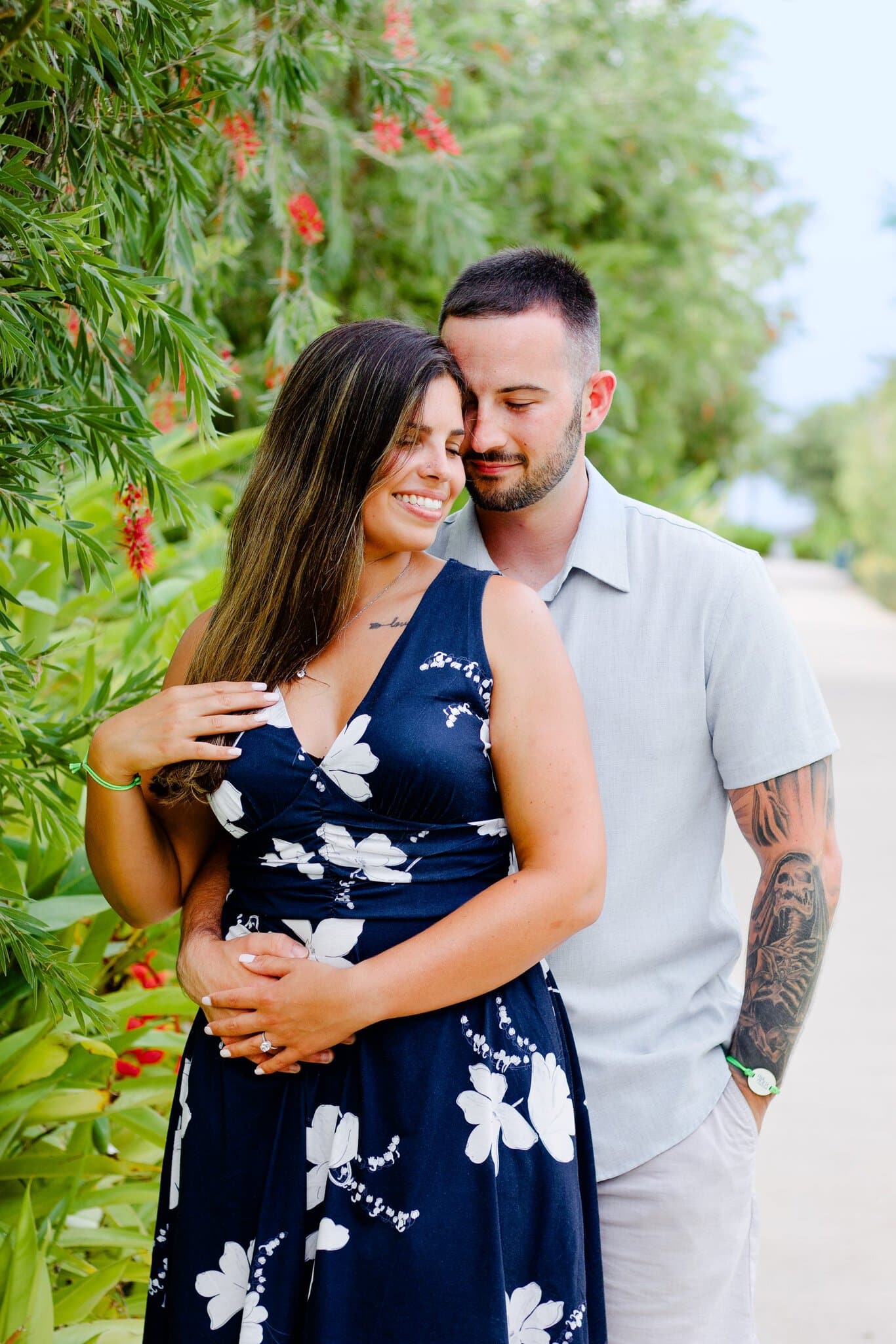 Engaged woman resting her head on her fiance with her ring hand on his chest in a tropical garden