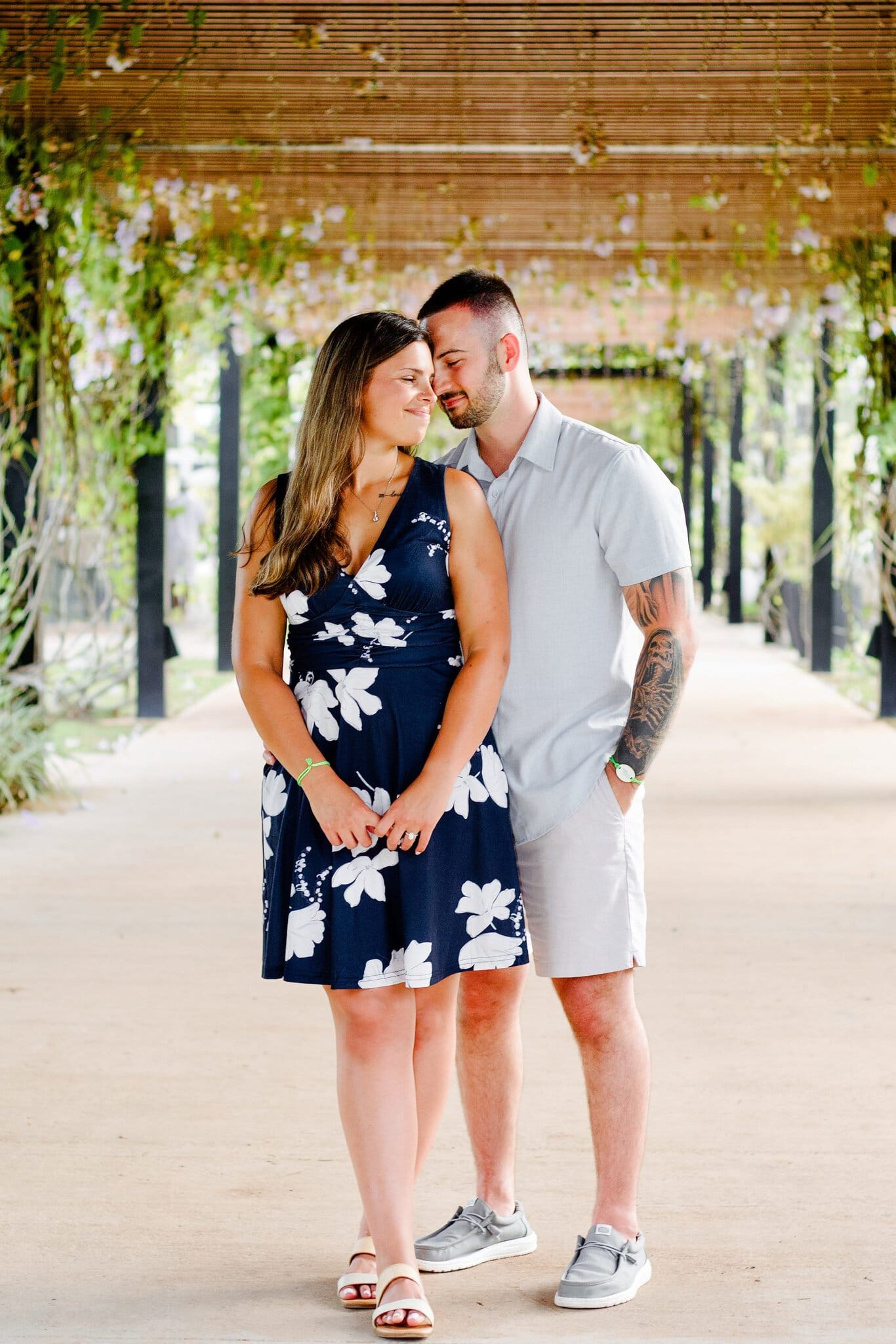 Engaged couple forehead to forehead under a flowering pergola walkway