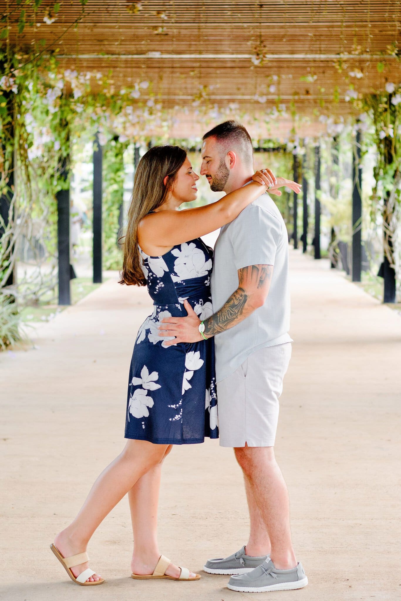 Woman wrapping her arm around her fiance as they lean in under a flowered walkway