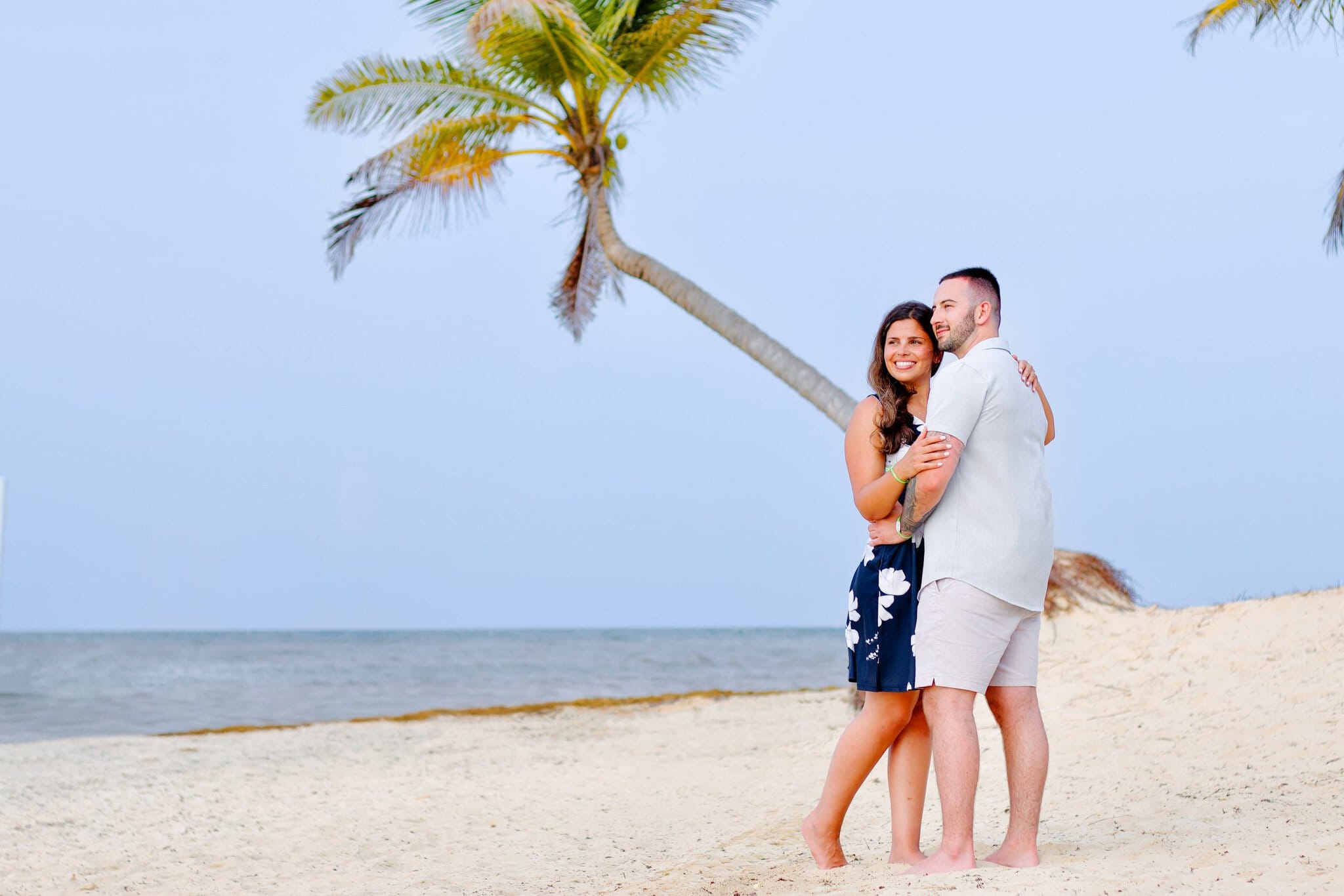 Newly engaged couple embracing under a leaning palm tree on the beach at Live Aqua Punta Cana