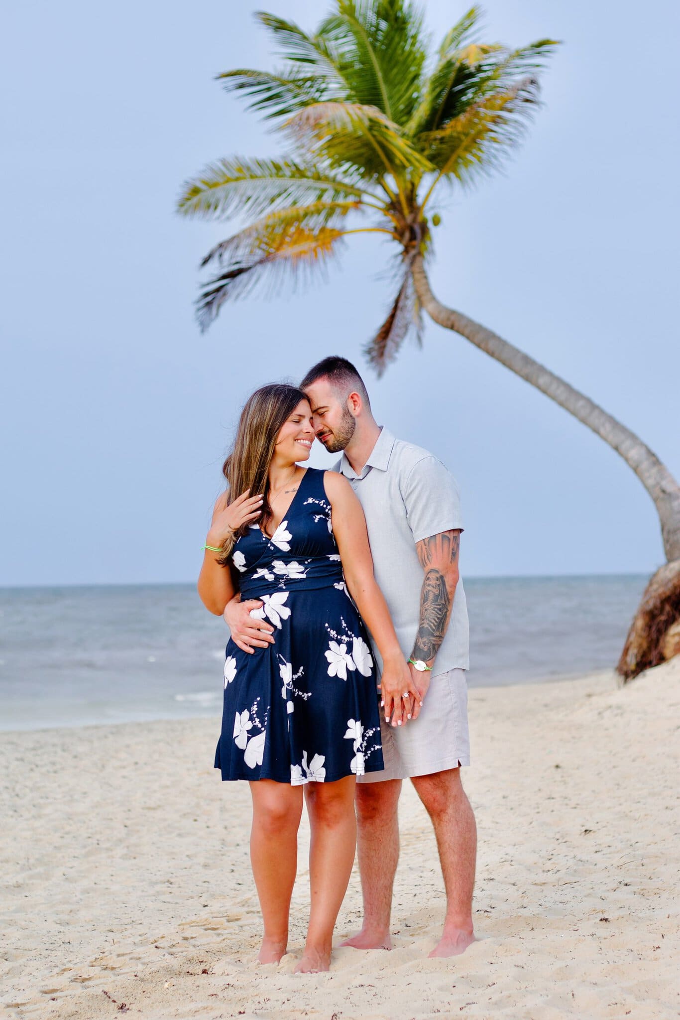 Newly engaged couple embracing under a palm tree at sunset on a Punta Cana beach
