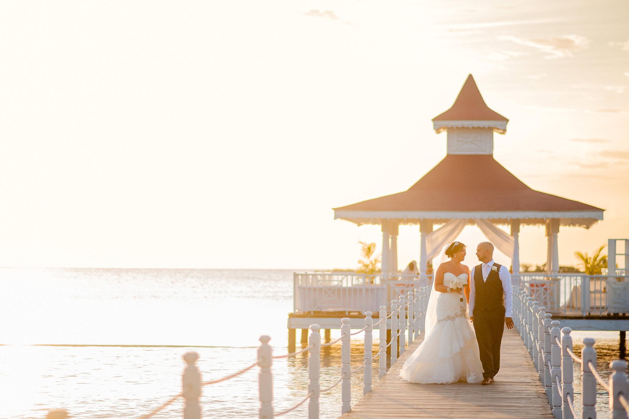 Bride and groom walking the pier towards the oceanfront gazebo at Bahia Principe La Romana, Dominican Republic