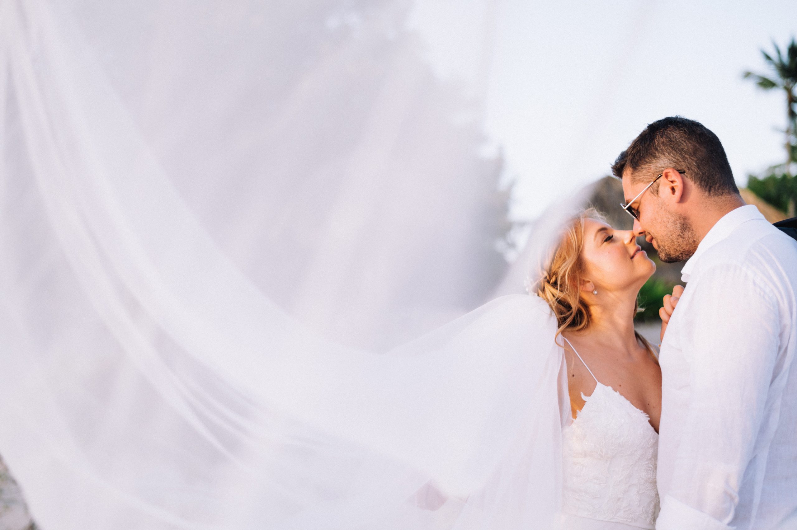 Bride and groom leaning toward each other as the bride’s veil sweeps across the foreground in Bayahibe