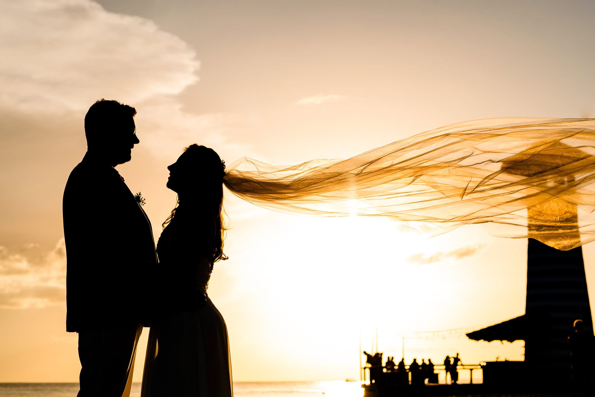 Bride and groom silhouetted at sunset with her veil lifting in the wind at a Bayahibe wedding, Dominican Republic