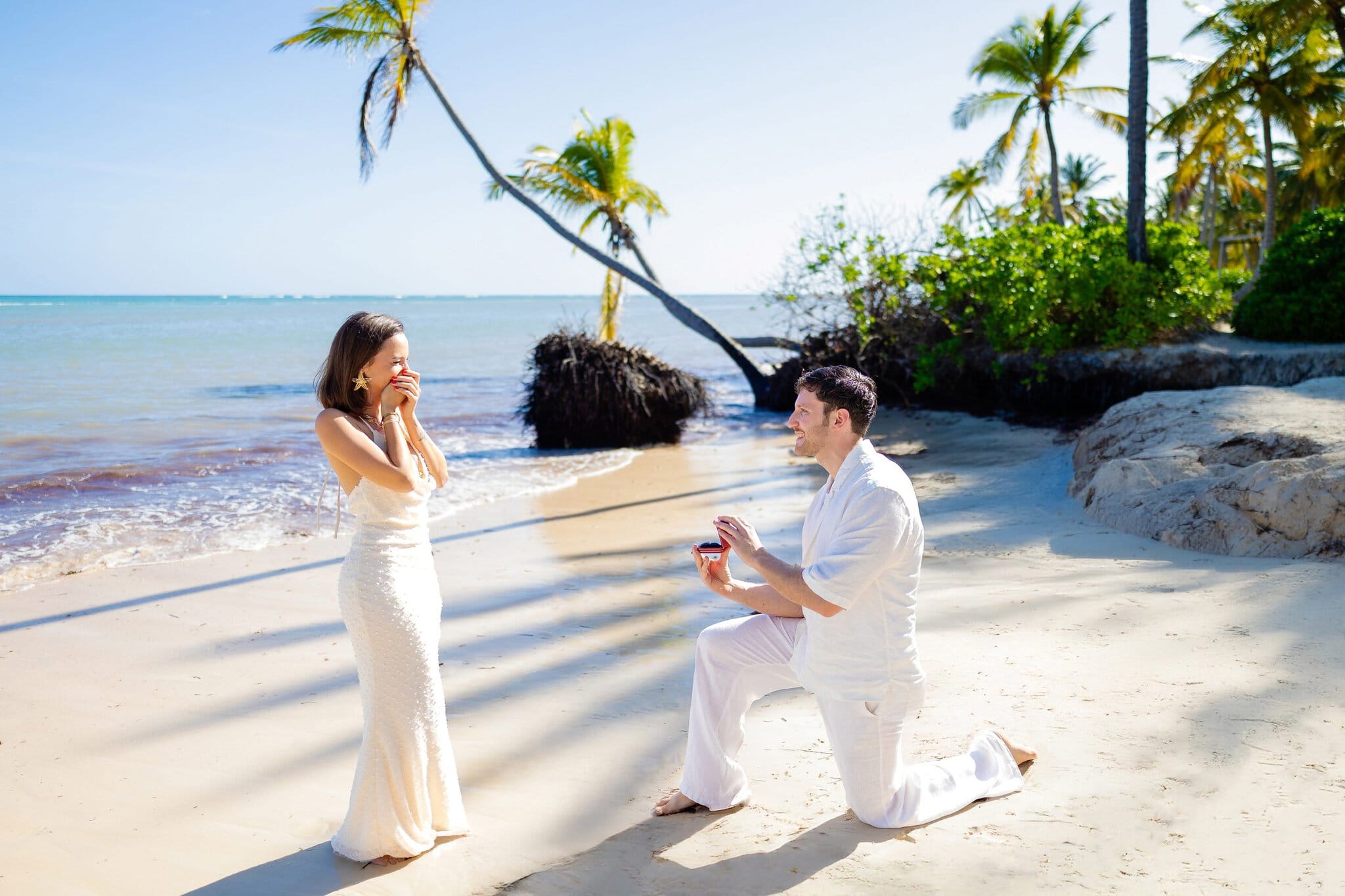 Man proposing on one knee as his surprised partner reacts on the beach