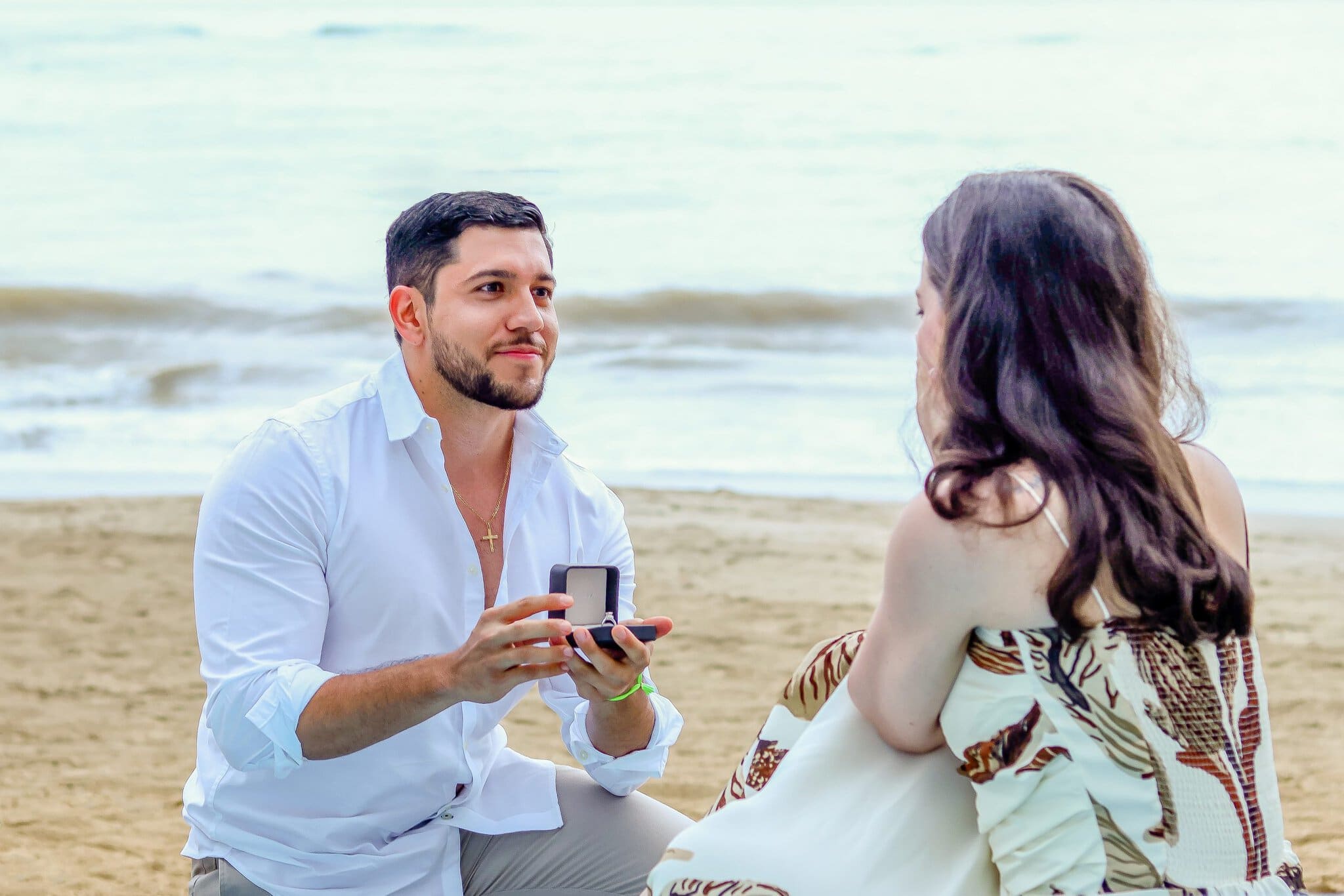 Man kneeling on the beach and presenting an engagement ring to his partner