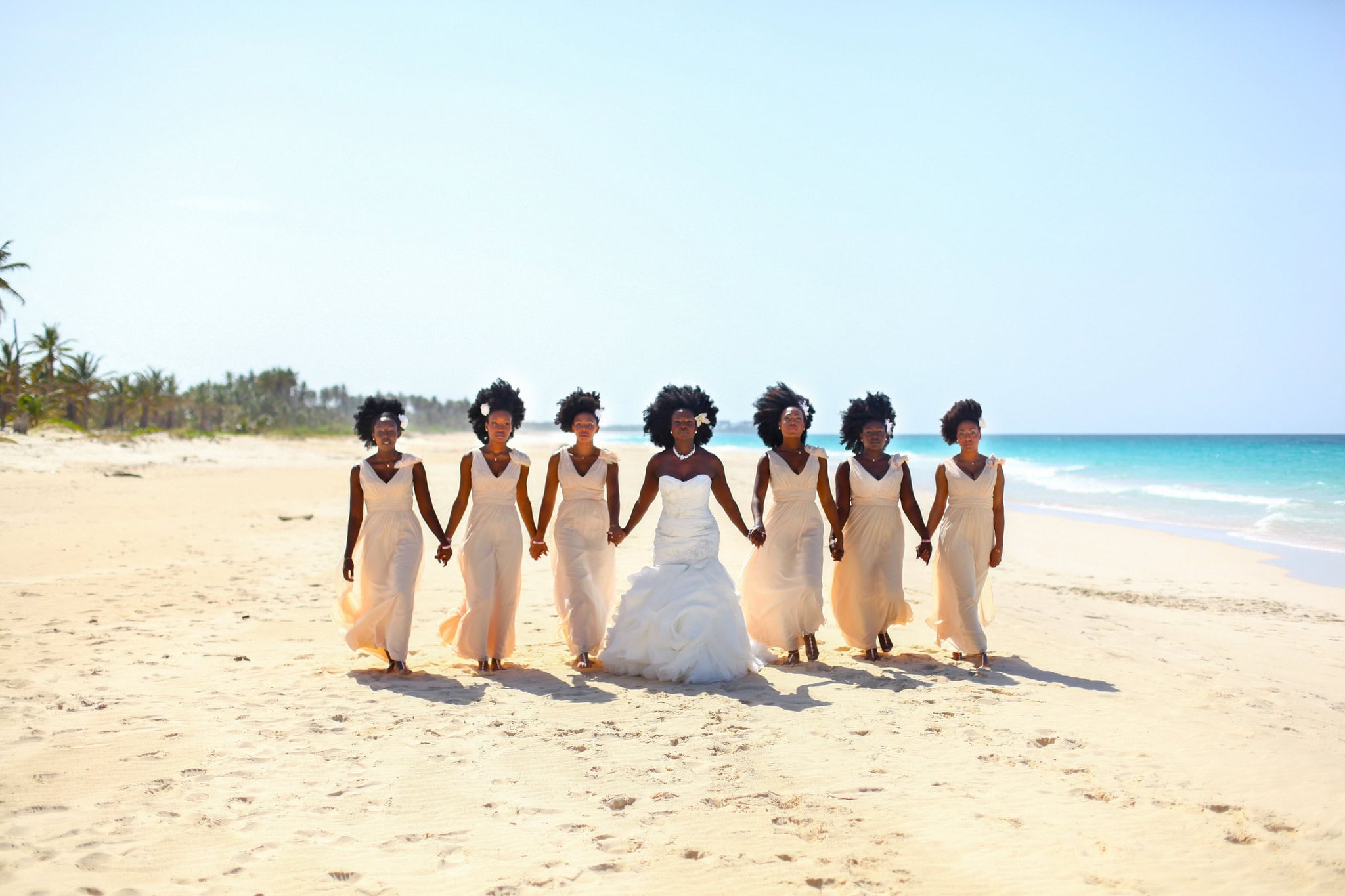 Bride walking hand in hand along the beach with her bridesmaids in matching gowns at a Punta Cana wedding