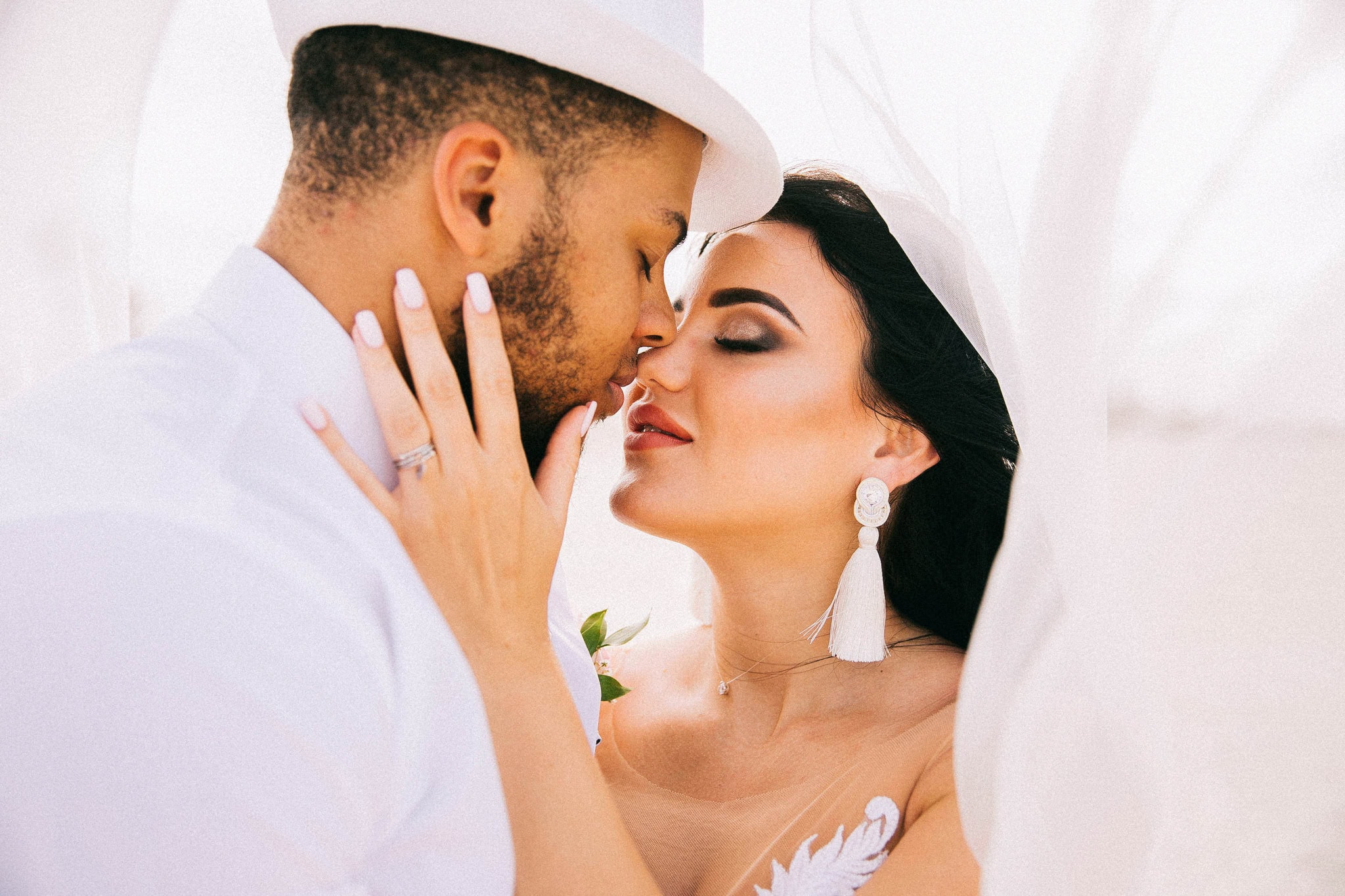 Bride and groom leaning in to kiss under her veil, both dressed in white, at a Punta Cana wedding