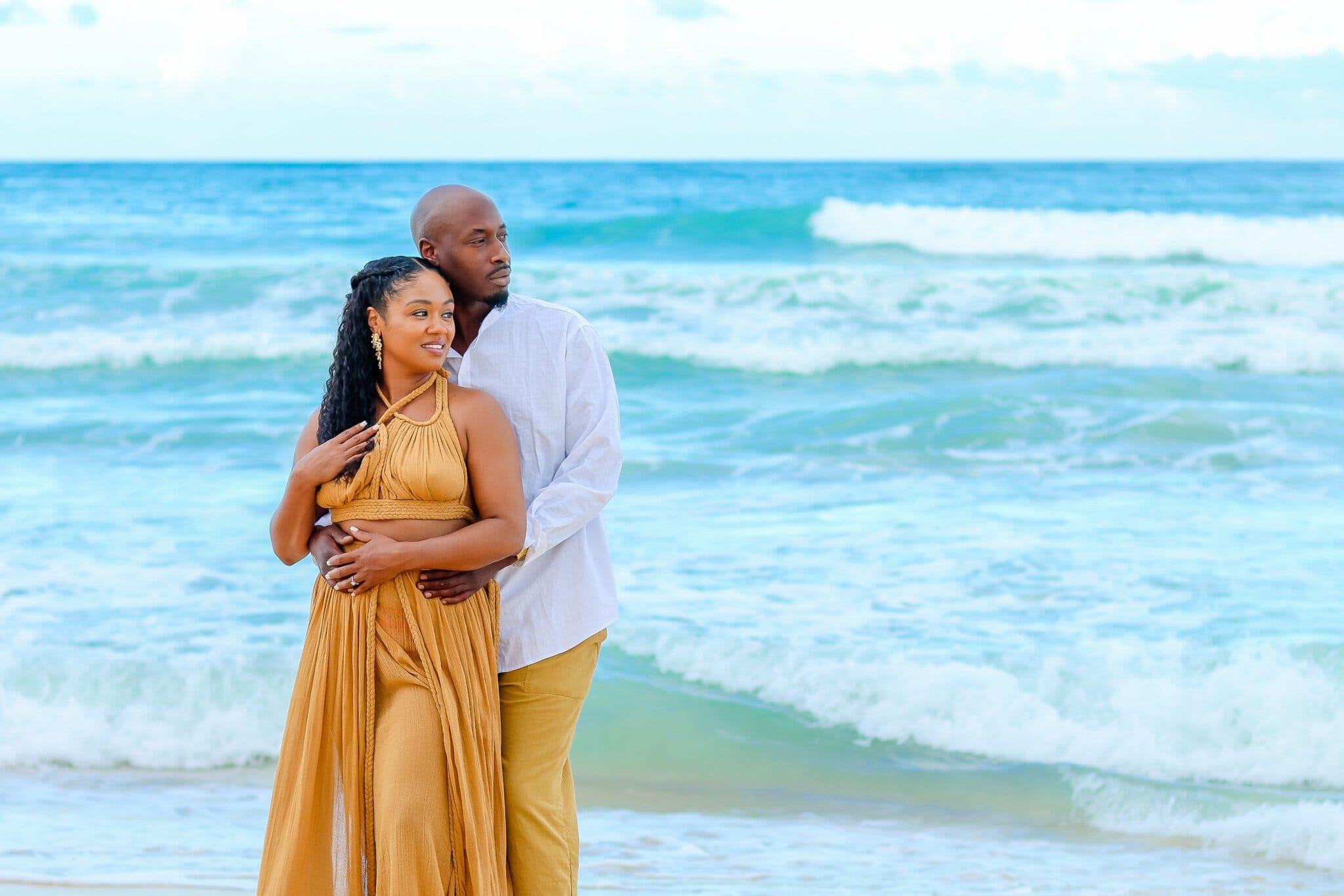 Couple standing by the ocean as one partner embraces the other from behind