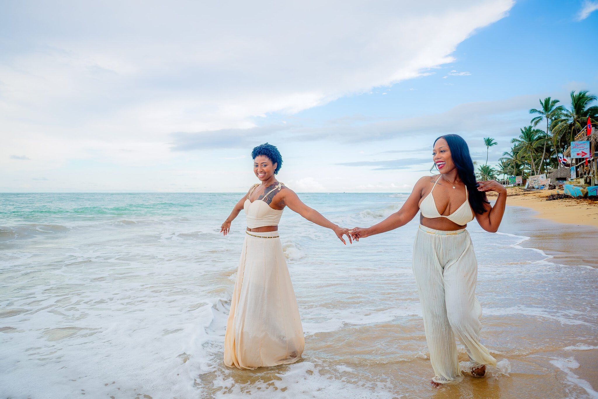 Couple holding hands and smiling while walking through shallow ocean water during a beach photo session