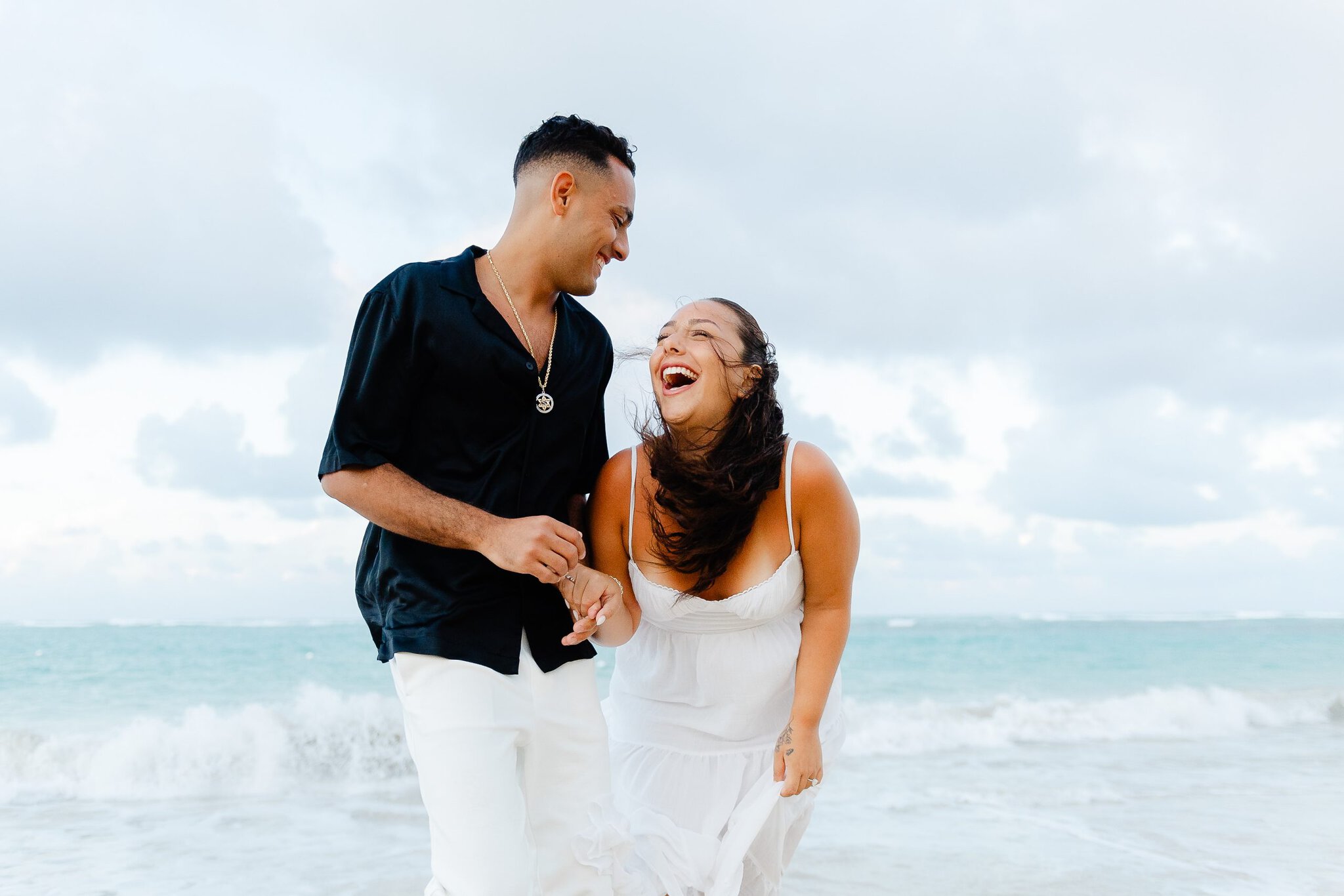 Couple holding hands and laughing together during a relaxed beach photo session