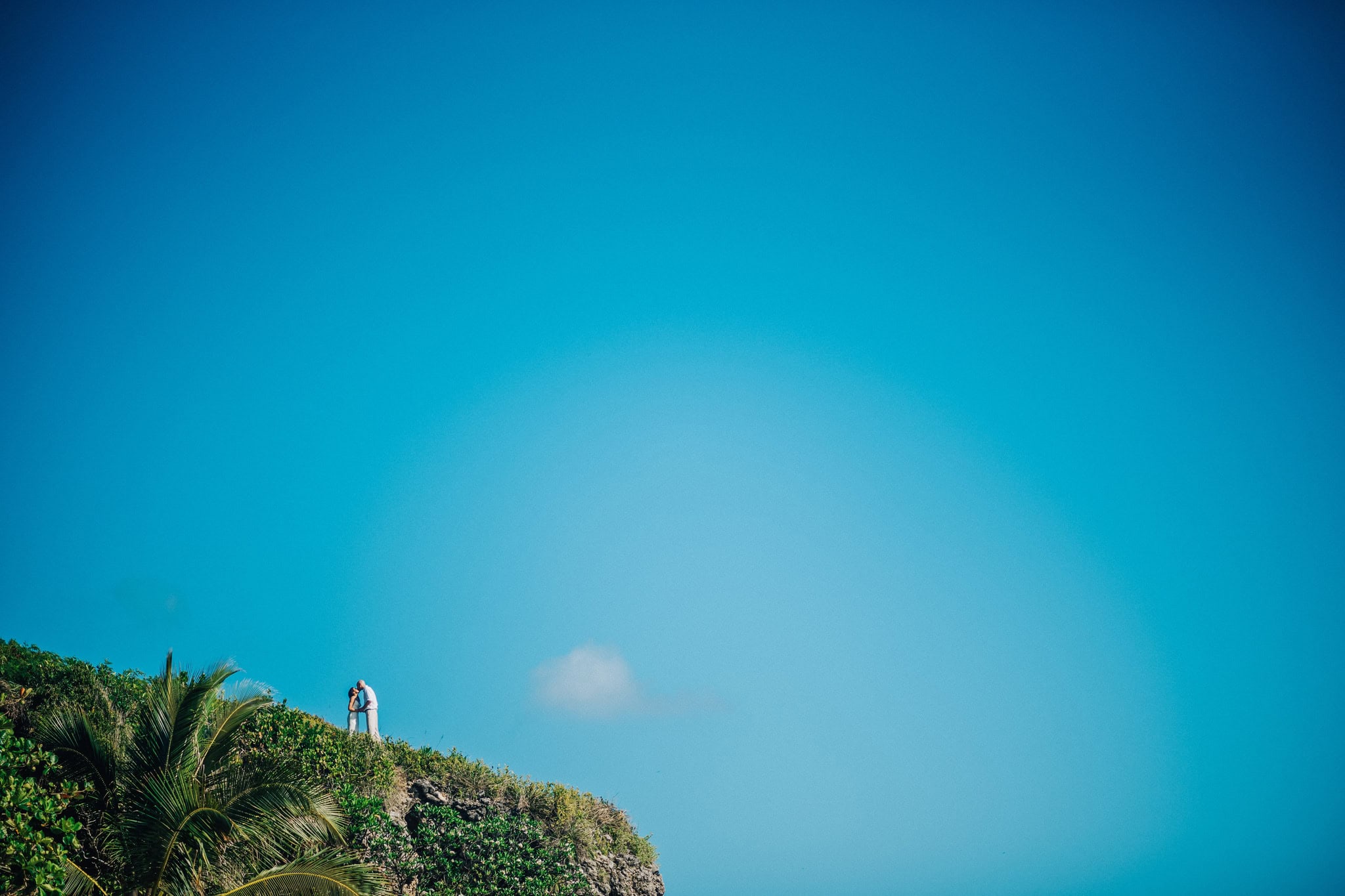 Bride and groom standing together on a green clifftop high above the sea under a wide blue sky in Cabrera, Dominican Republic
