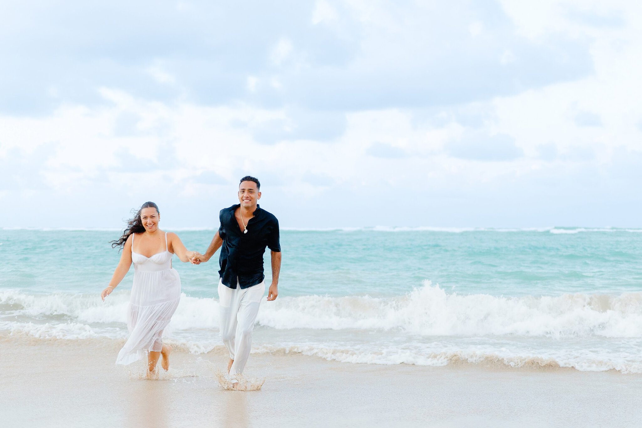 Couple holding hands and running through shallow ocean waves during a beach photo session