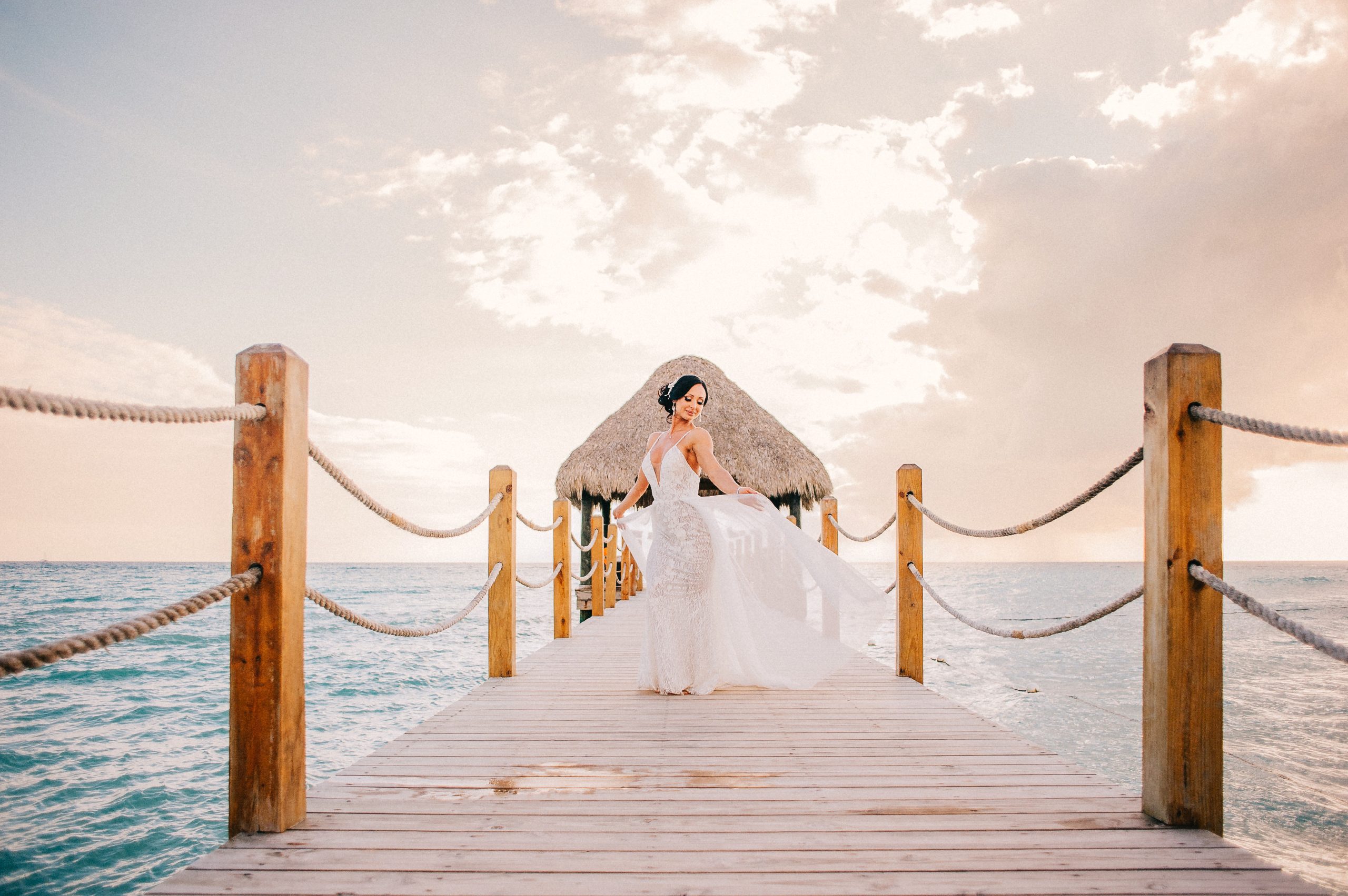 Bride holding the train of her dress on a wooden ocean pier at Dreams Dominicus in Bayahibe