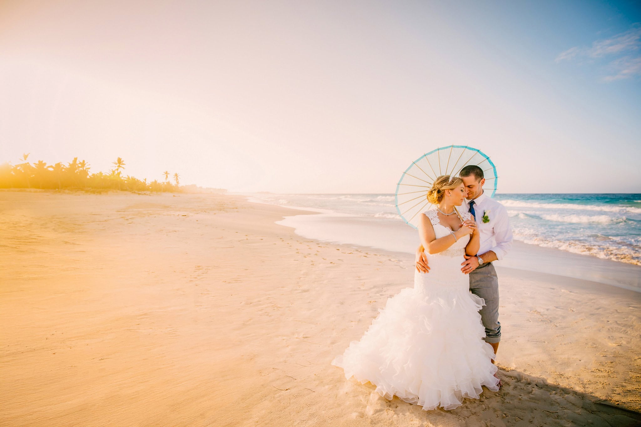 Bride and groom under a paper parasol on the beach at golden hour during an elopement in Punta Cana