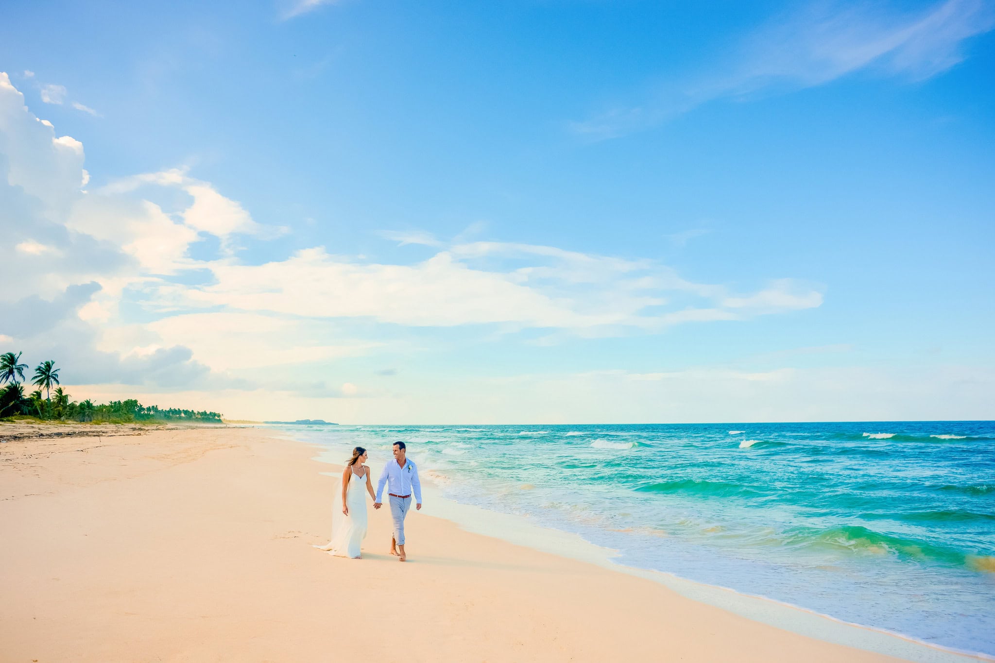 Eloping couple walking hand in hand along a wide empty beach in Punta Cana, Dominican Republic