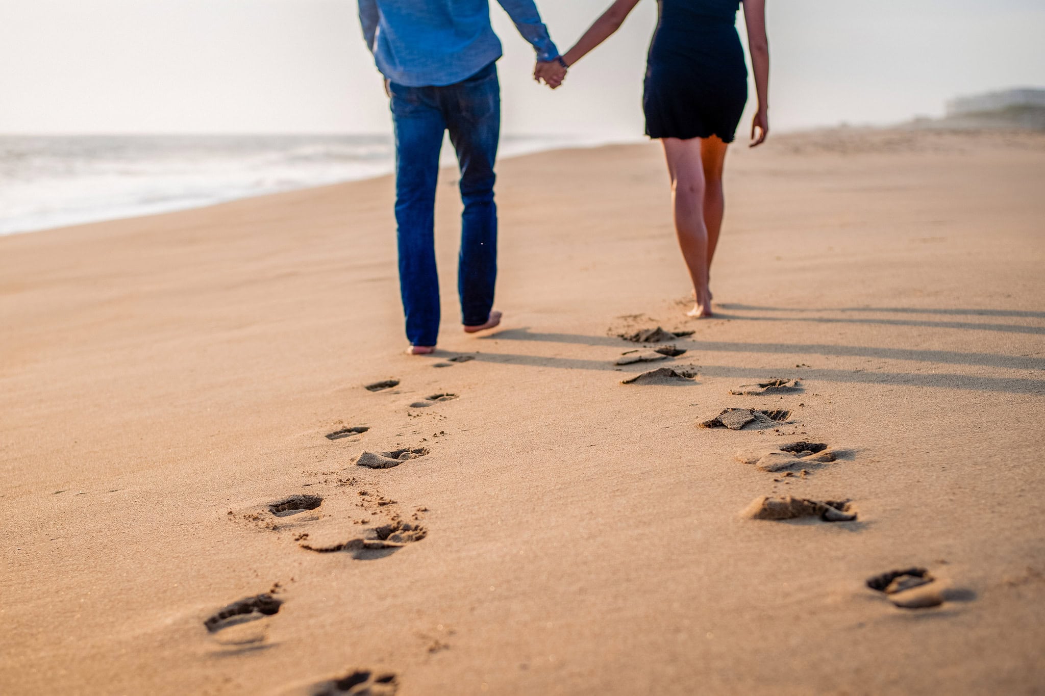 Couple walking hand in hand along the beach leaving footprints in the sand during an engagement session in Punta Cana