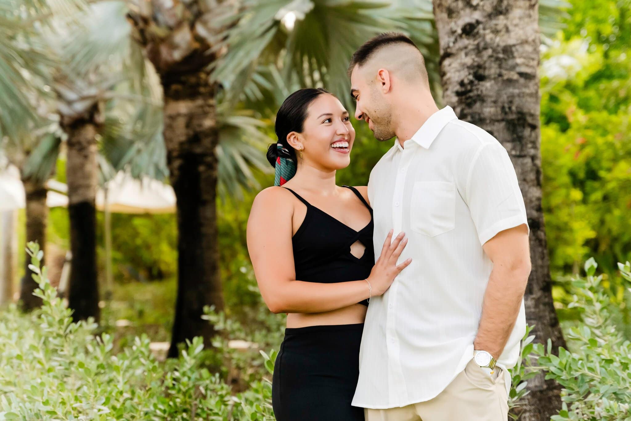 Engaged couple smiling at each other during a relaxed outdoor portrait session among palm trees