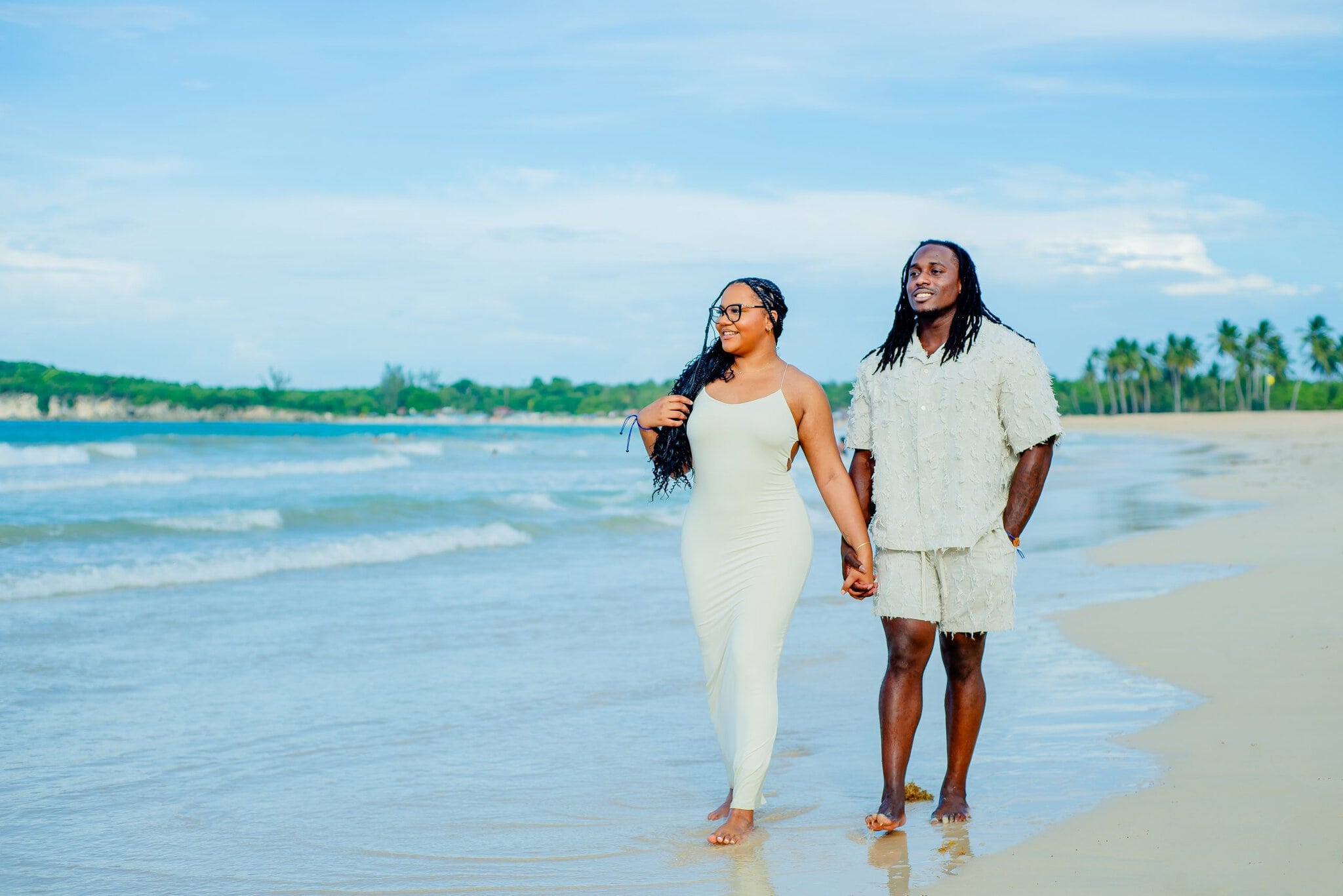 Engaged couple holding hands while walking barefoot along the shoreline during their photo session