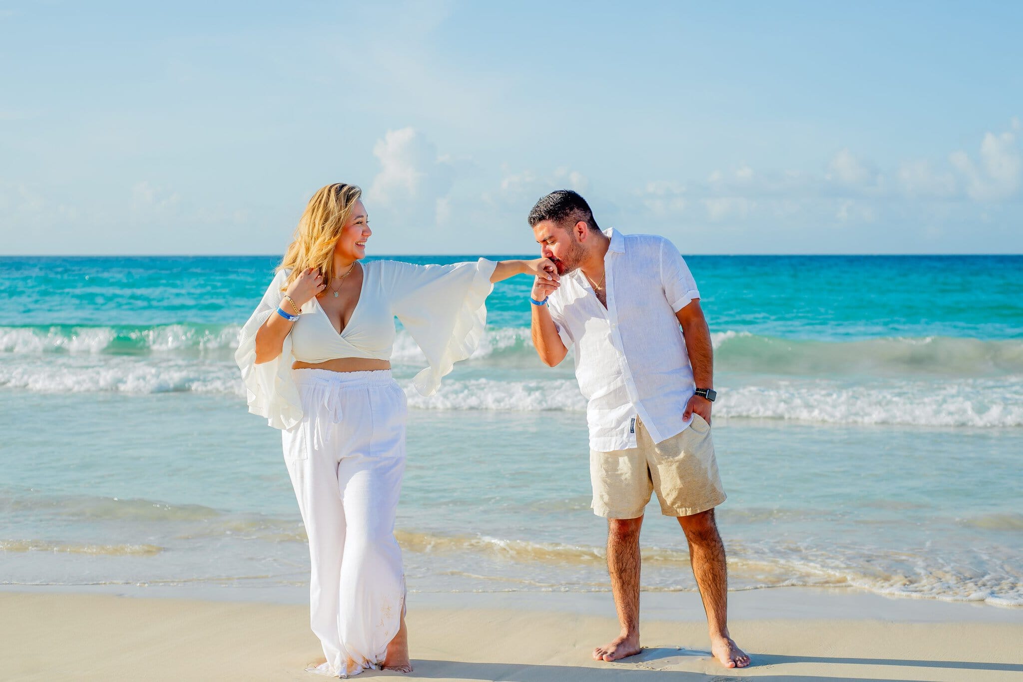 Engaged couple smiling as he kisses her hand during a relaxed beach photo session