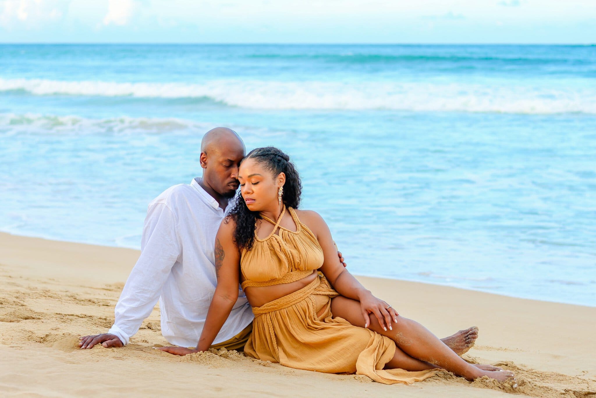 Engaged couple sitting close together on the sand during a relaxed beach portrait session