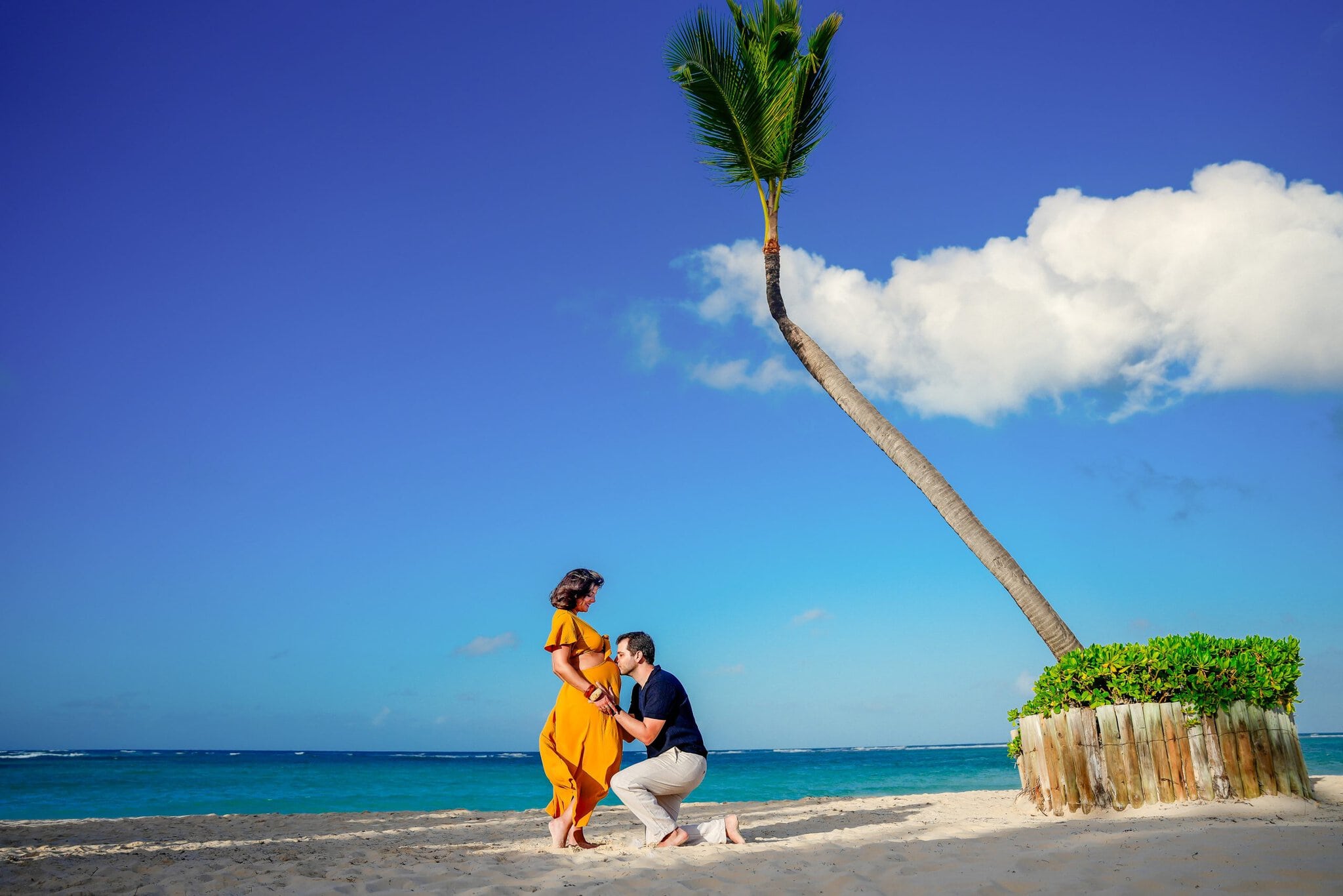 Expectant couple on the beach as the partner kisses the pregnant woman’s belly
