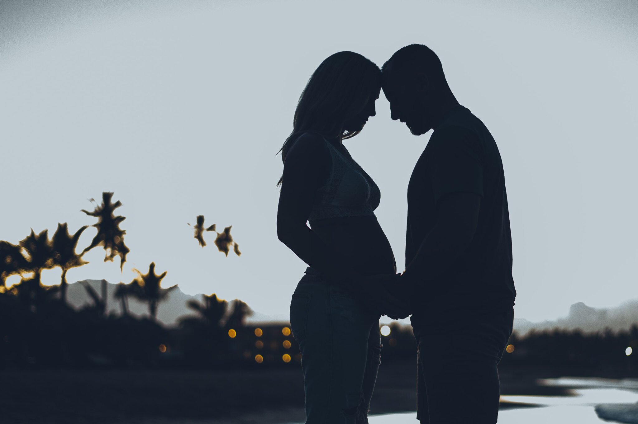 Expectant couple touching foreheads and holding the baby bump in a maternity silhouette portrait