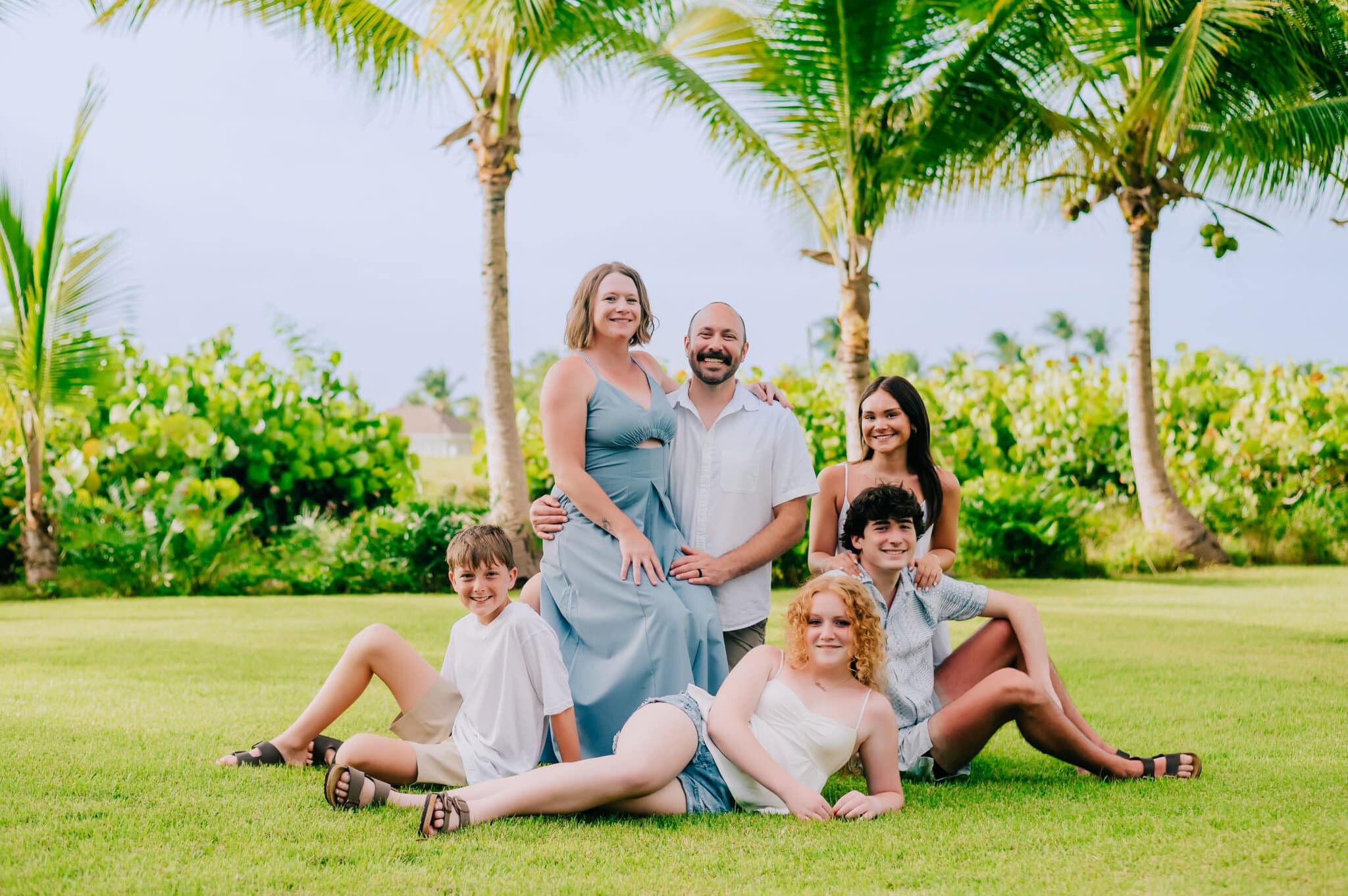 Family of six posing together on a lawn beneath palm trees