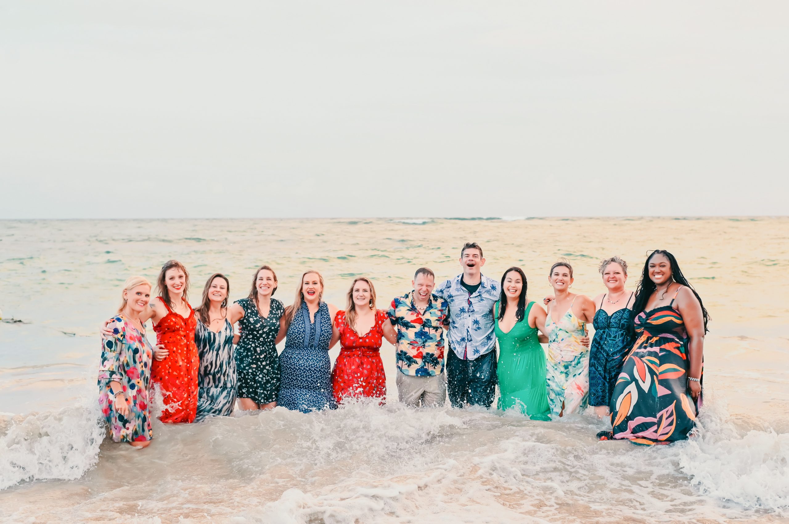 Large family group smiling together in colorful outfits as waves wash around them at the shoreline