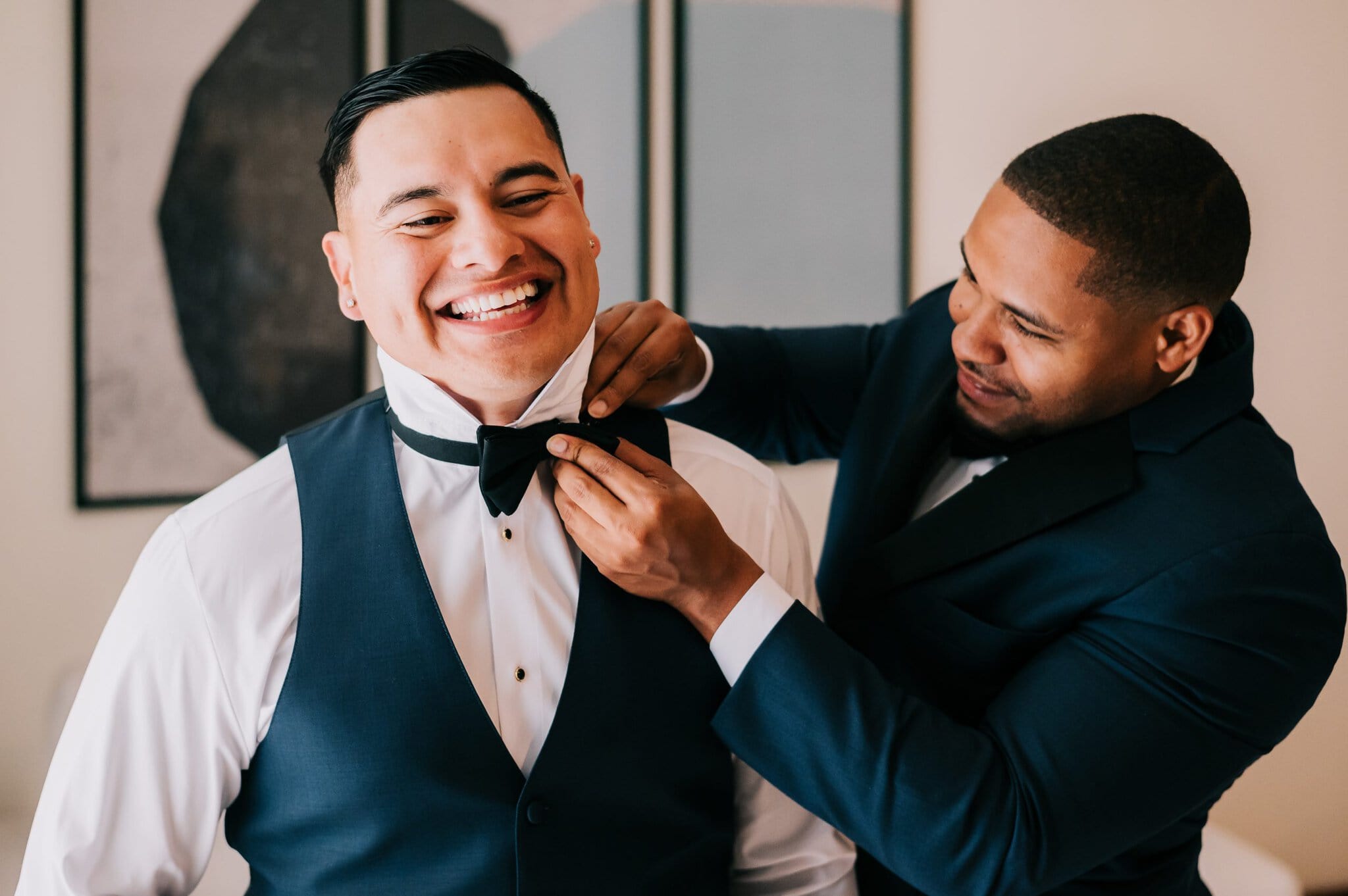 Groomsman adjusting the groom’s bow tie while they get ready for the wedding